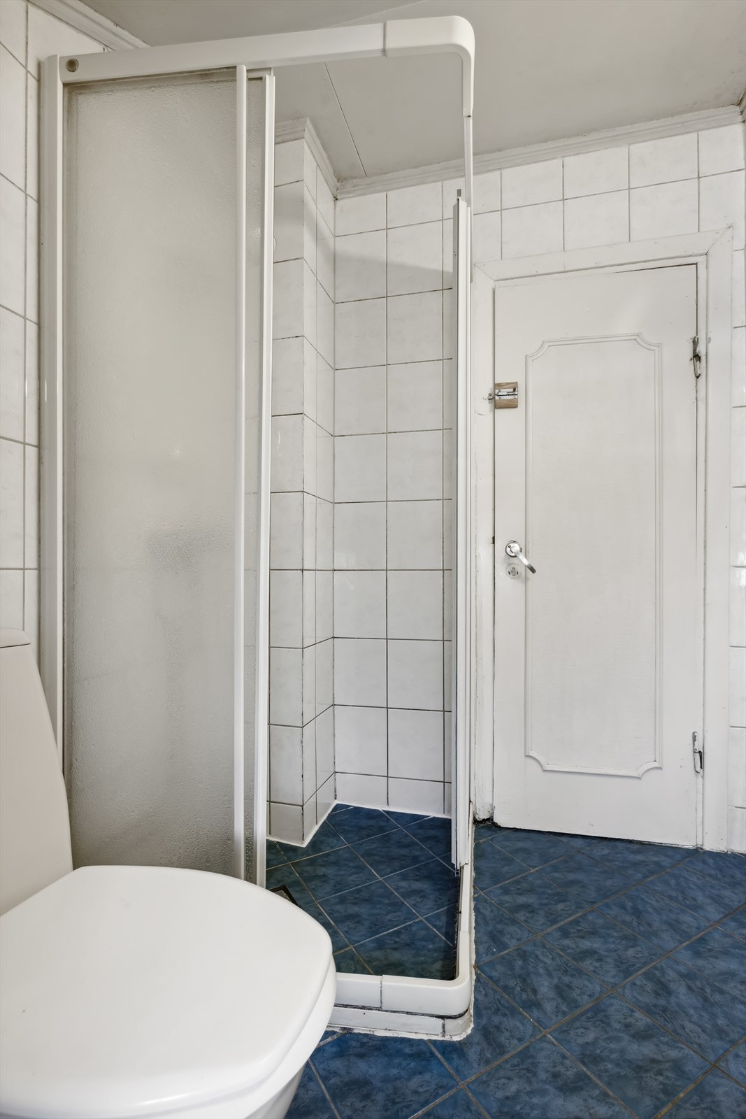 Flislagt baderom innredet med enkel servant, frittstående toalett og dusjhjørne. Galleribilde