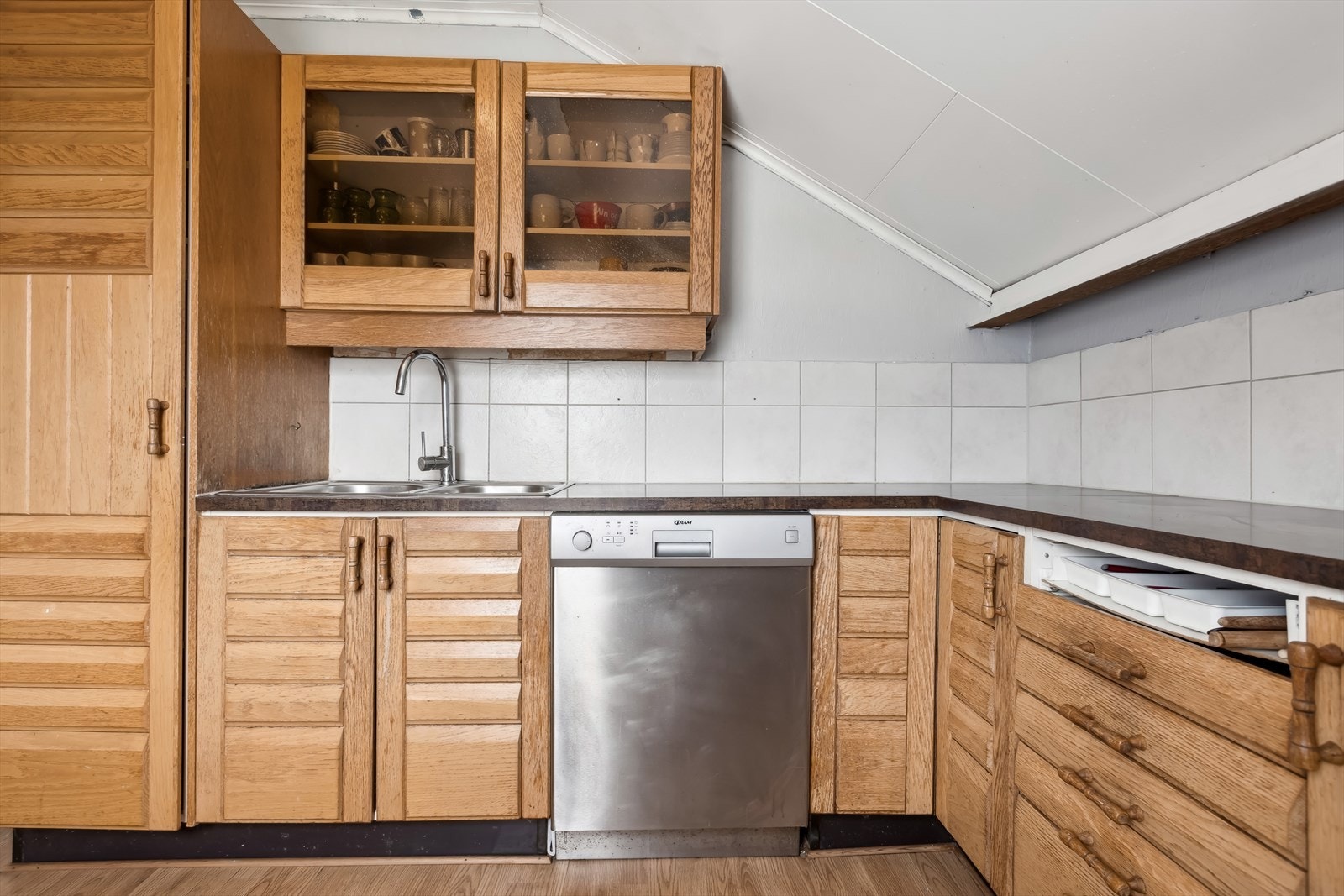 Kjøkkeninnredning med eikefronter og laminat benkeplate. Fliser over benk. Frittstående komfyr, oppvaskmaskin, kjøleskap og fryseboks. Galleribilde