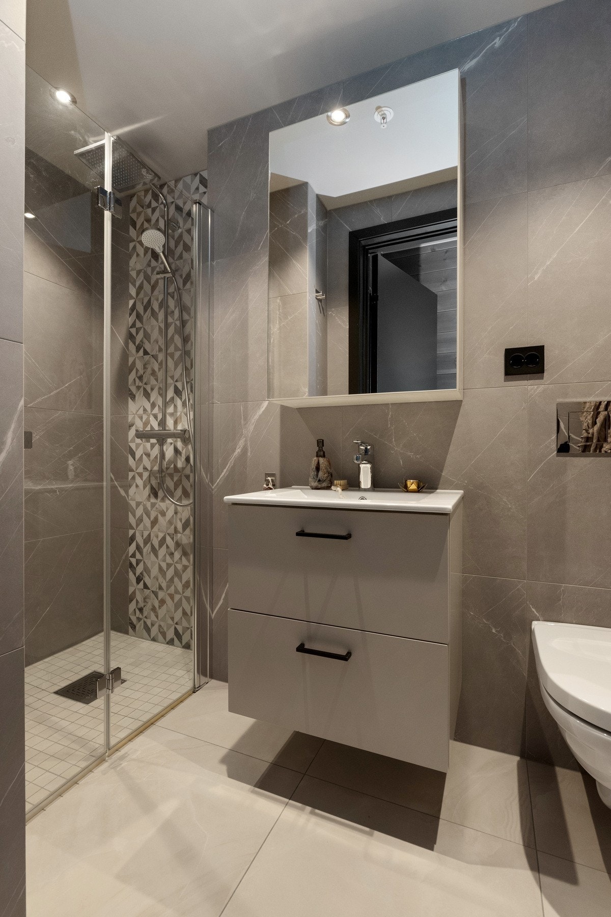 Adkomst til privat delikat bad med store fliser på gulv og vegg. I dusjnisjen har den ene veggen fliser med mønster som løfter Galleribilde