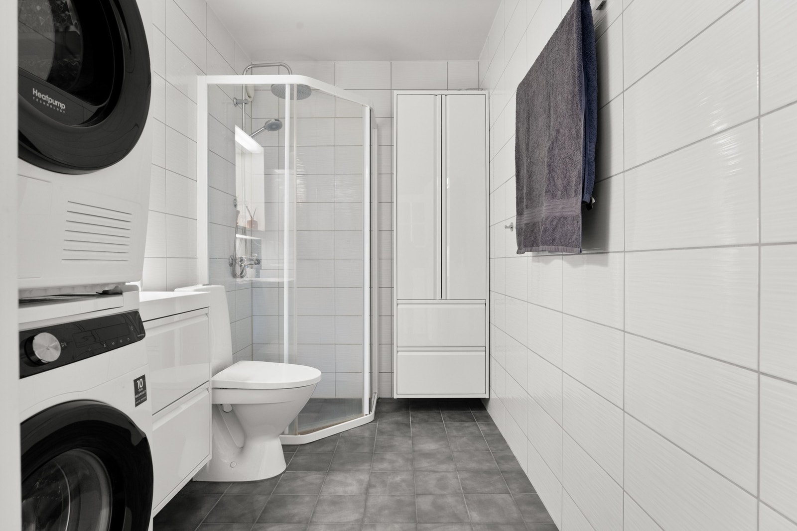 Badet fremstår som velholdt og pent, med hvite fliser på veggene og grå fliser på gulv med elektrisk gulvvarme. Galleribilde