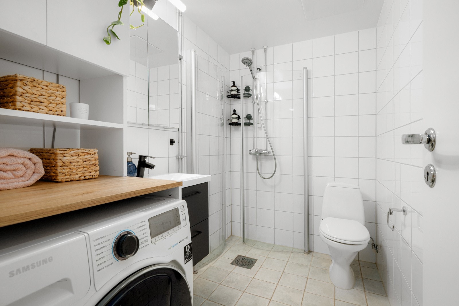 Leiligheten har et lyst flislagt baderom fra byggeåret 2006. I hjørnet av baderommet er det plass og opplegg for vaskemaskin i en praktisk innredning med benkeplate, hylle og skap. Galleribilde