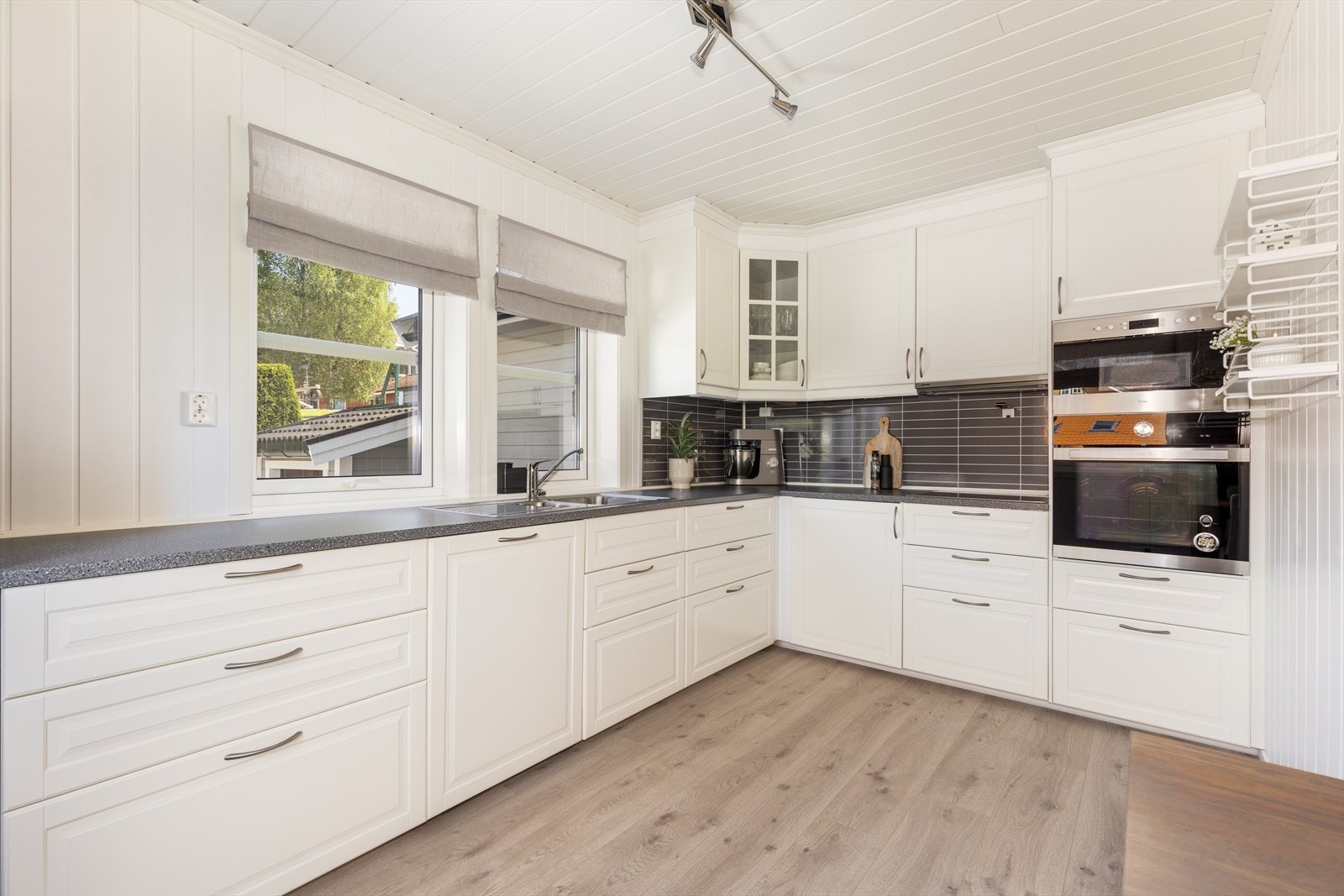 Kjøkkenet har en stilren, hvit innredning med profilerte fronter. Gode arbeidsflater på laminat benkeplate med nedfelt oppvaskkum med to kummer og avrenningsflate og nedfelt induksjonstopp. Galleribilde