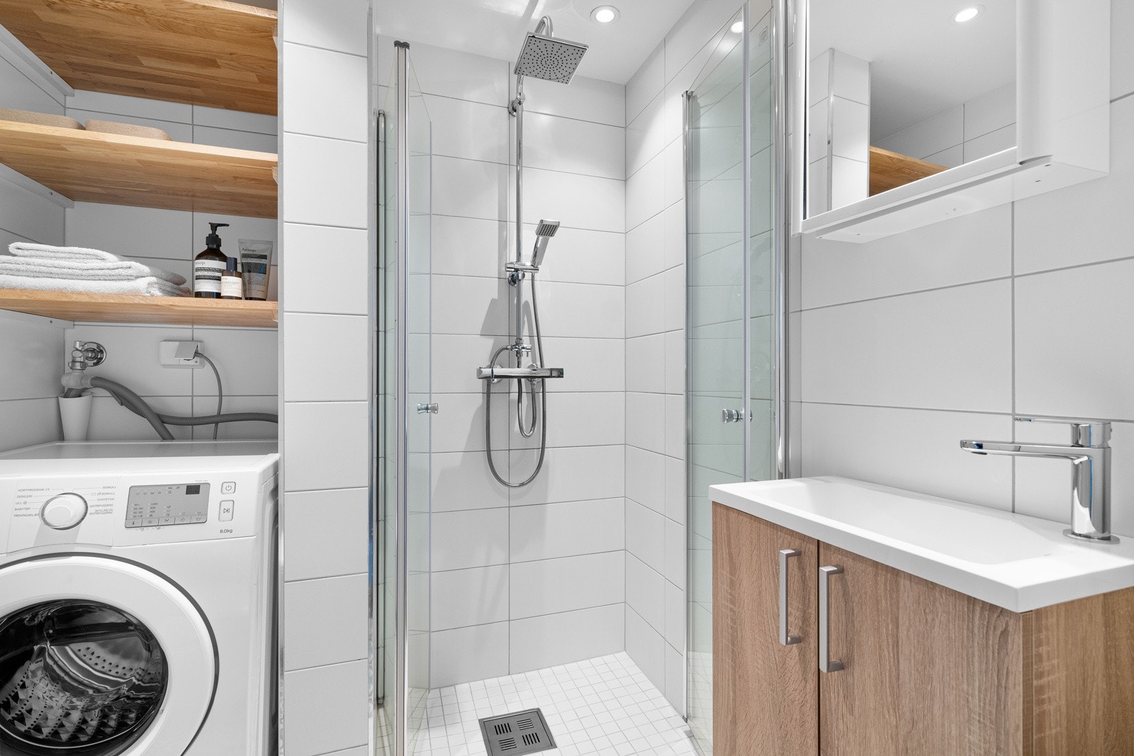 Baderommet inneholder servant med ett-greps armatur, speil, dusjhjørne, vegghengt toalett og opplegg for vaskemaskin. Galleribilde