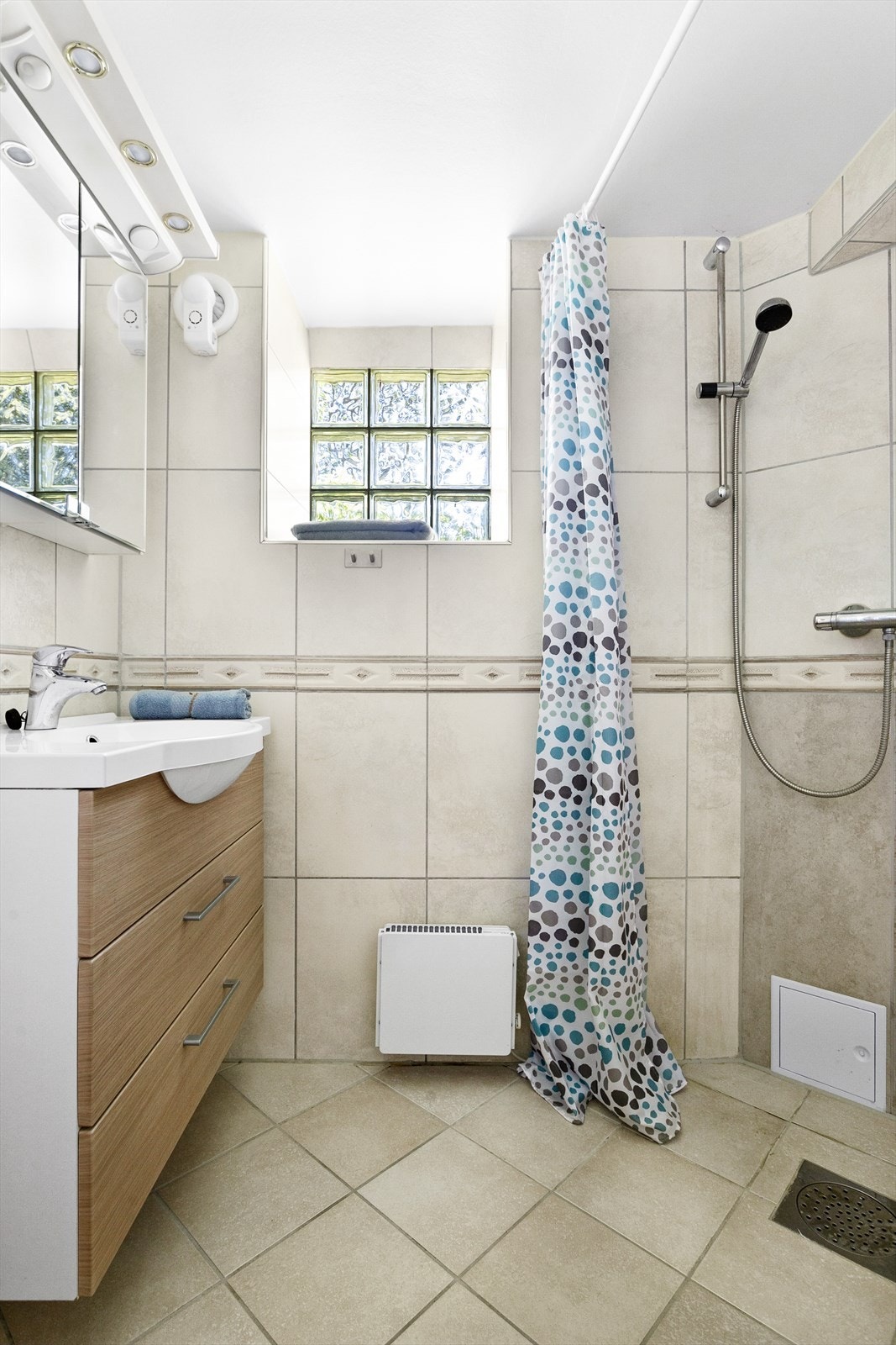 Flislagt bad med gulvvarme. Innredning av vegghengt servant, skapspeil over vask og dusjhjørne. Galleribilde