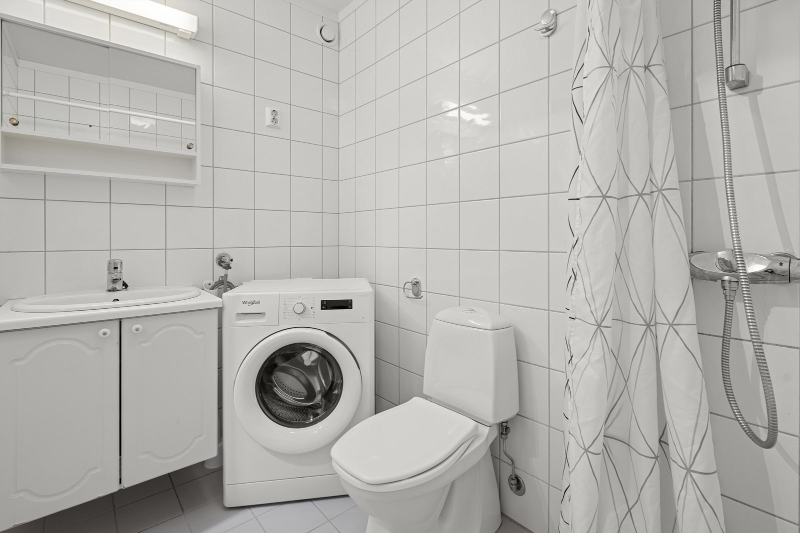 Rommet inneholder toalett, dusj med forheng, hvit servant nedfelt i baderomsinnredning og opplegg og plass for vaskemaskin Galleribilde