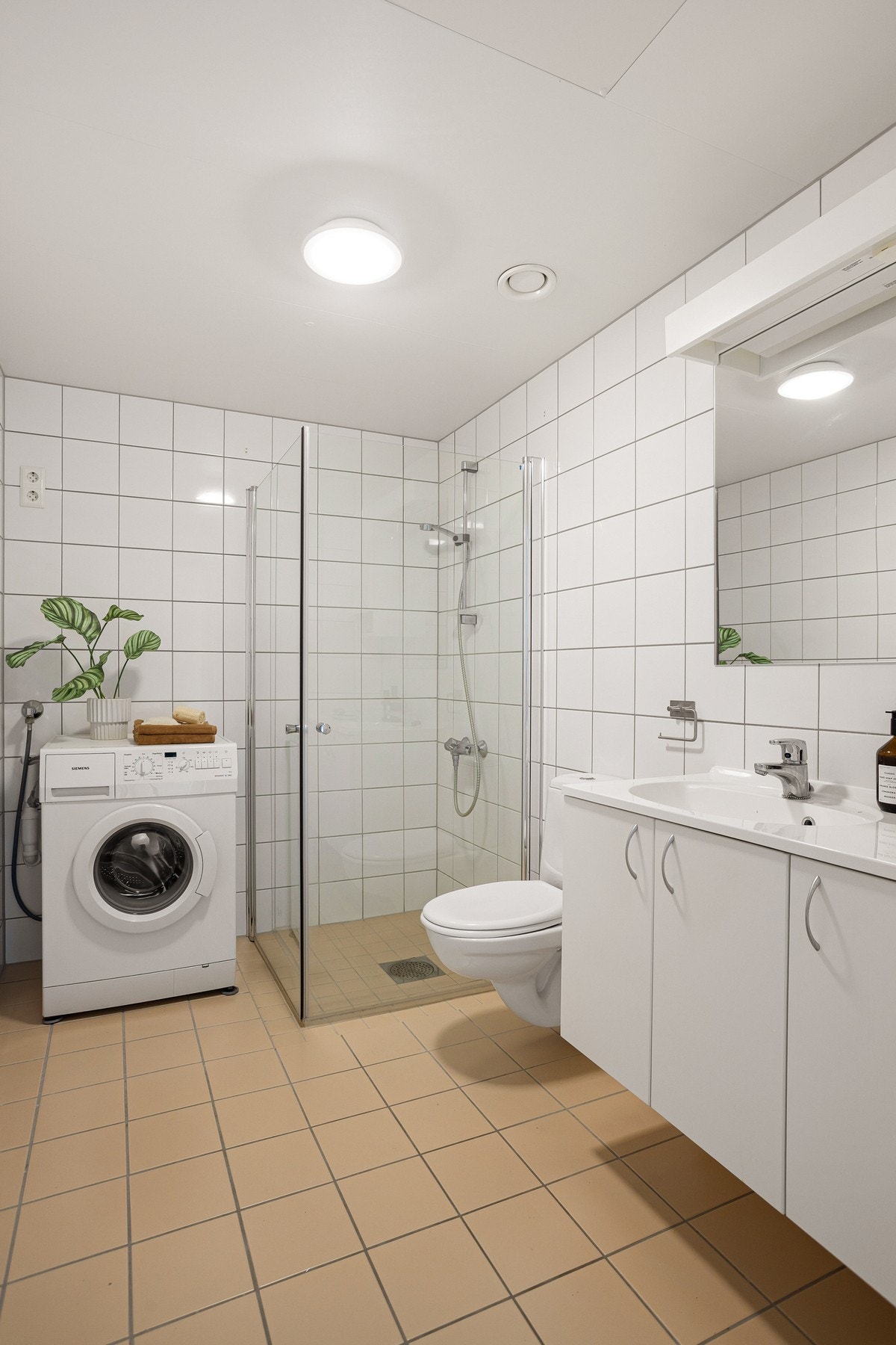 Boligen har et lyst bad med inngang fra entreen. Badet er bygget opp med hvite fliser på vegg med opplegg for vaskemaskin og tørketrommel. Galleribilde