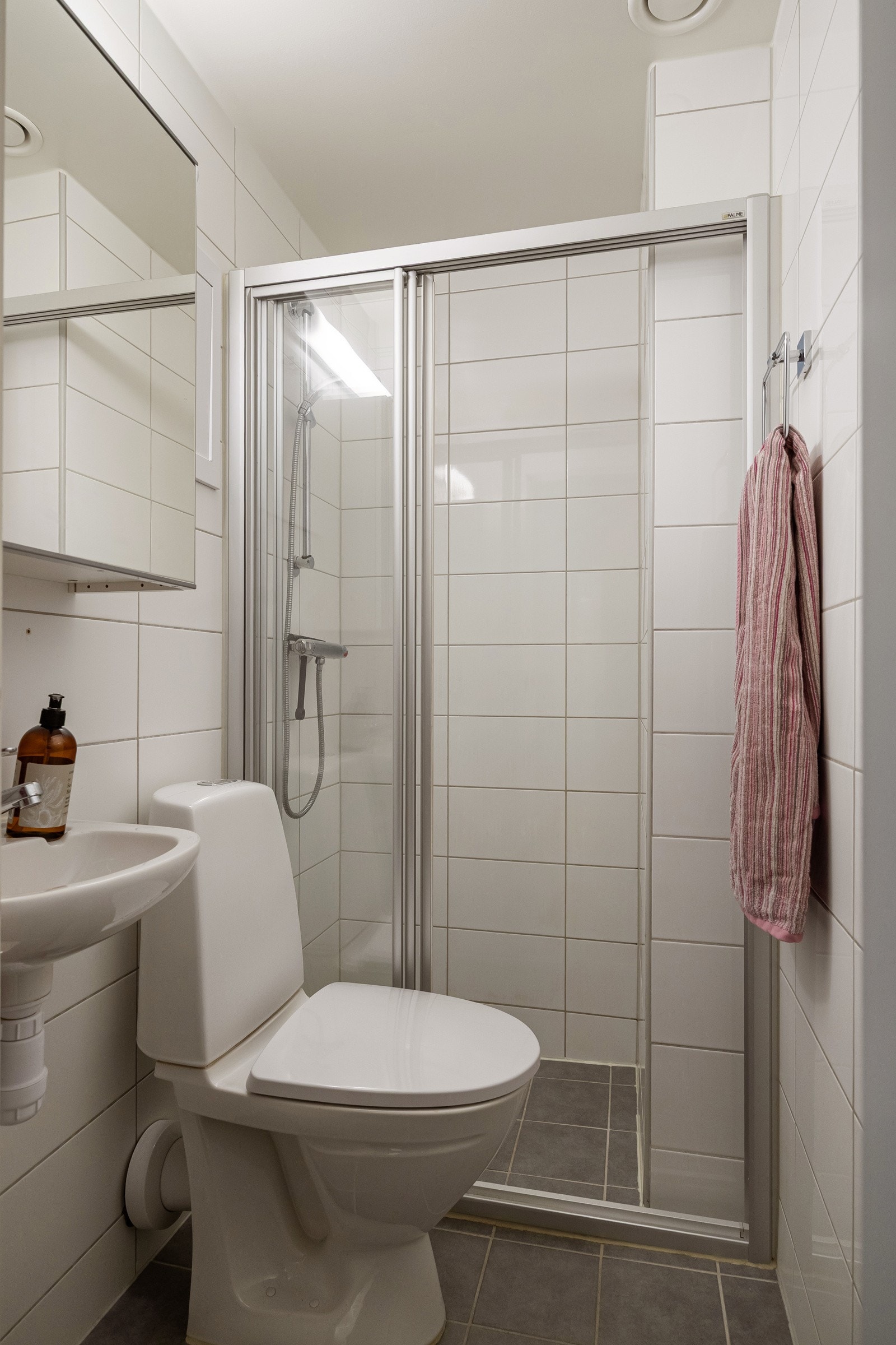 Baderommet har grå fliser på gulv med gulvvarme, hvite fliser på veggene og mekanisk avtrekk. Galleribilde