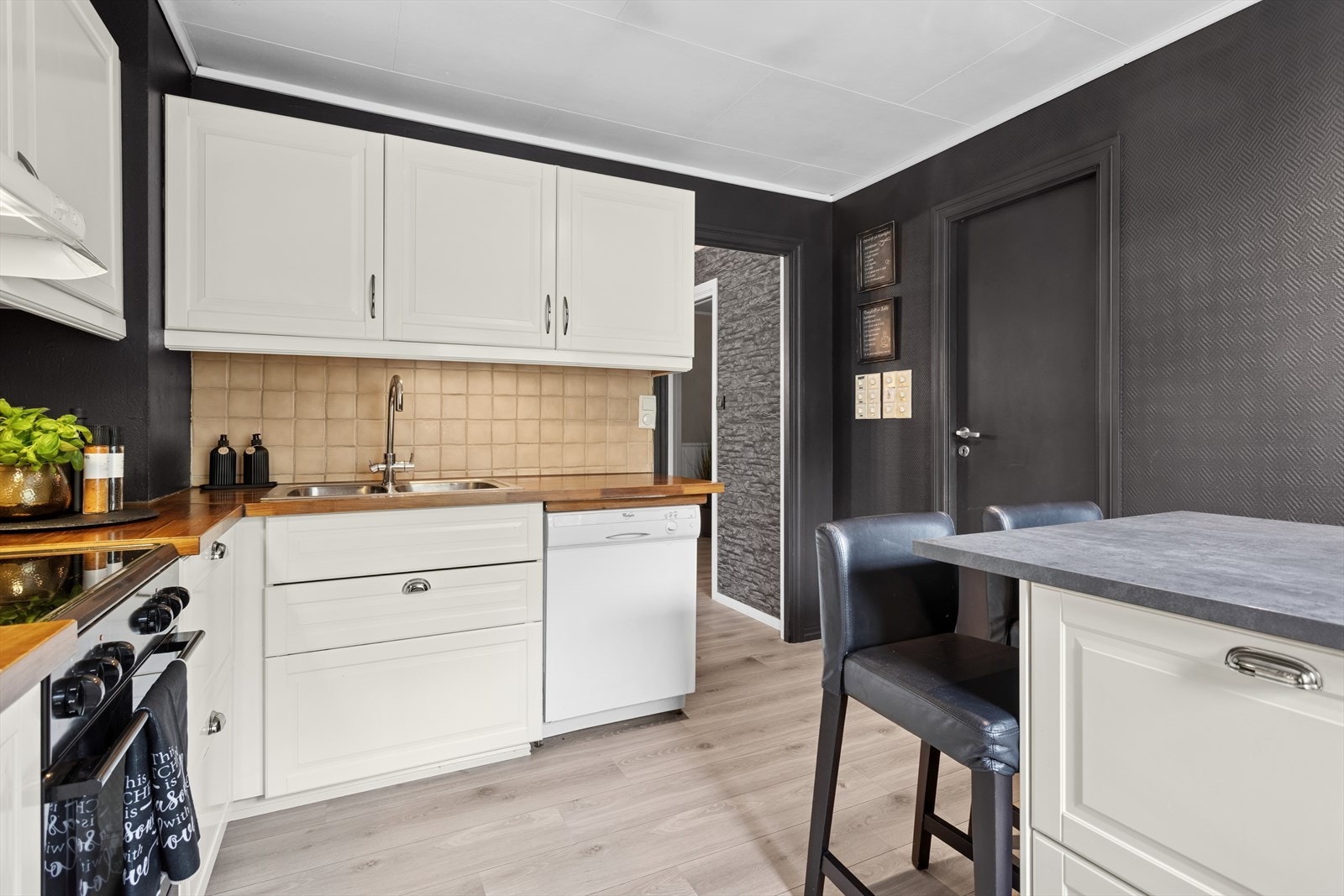 Kjøkkenets innredning har profilerte fronter, laminat benkeplate, fliser over benk og belysning under overskap. Galleribilde