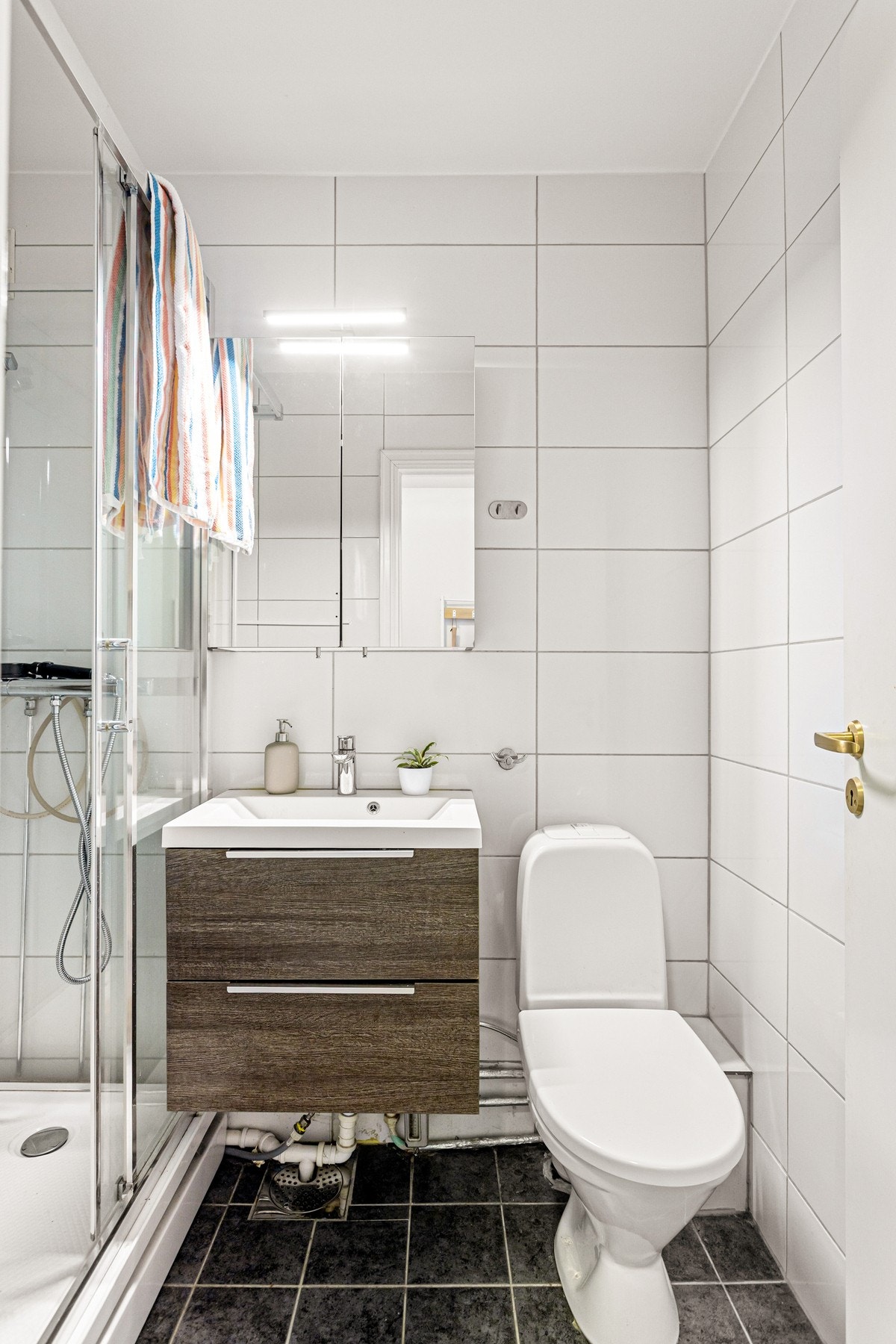 Badet er utstyrt med innredning med to skuffer og servant, toalett og dusjkabinett. Galleribilde