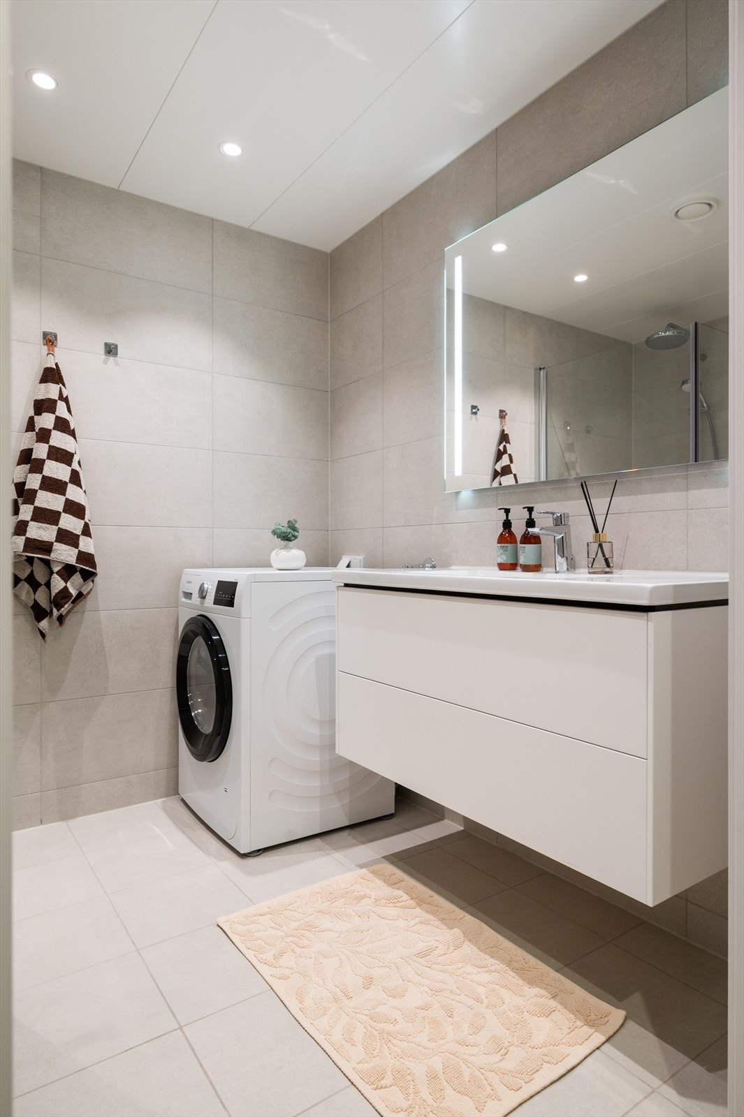 Servantinnredningen har hvite, glatte fronter, heldekkende porselensservant, ettgreps servantarmatur og speil med integrert belysning Galleribilde