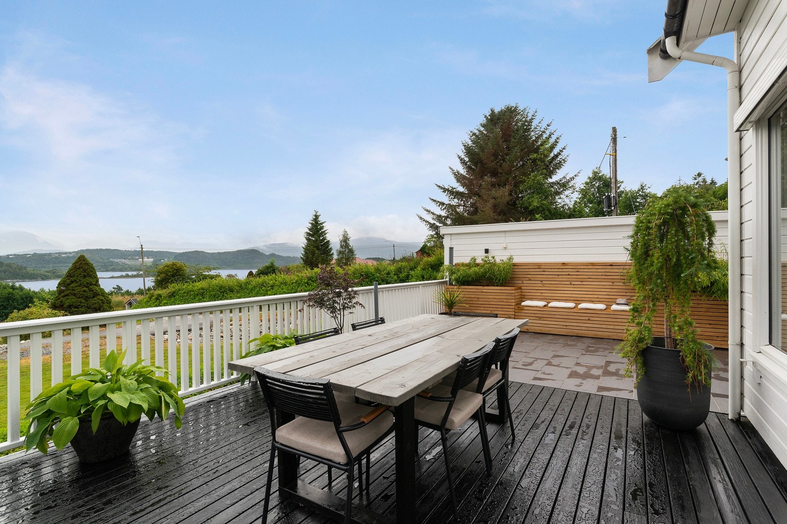 Det flislagte området er delvis overbygd og har integrerte plantekasser og benker i tre. Galleribilde