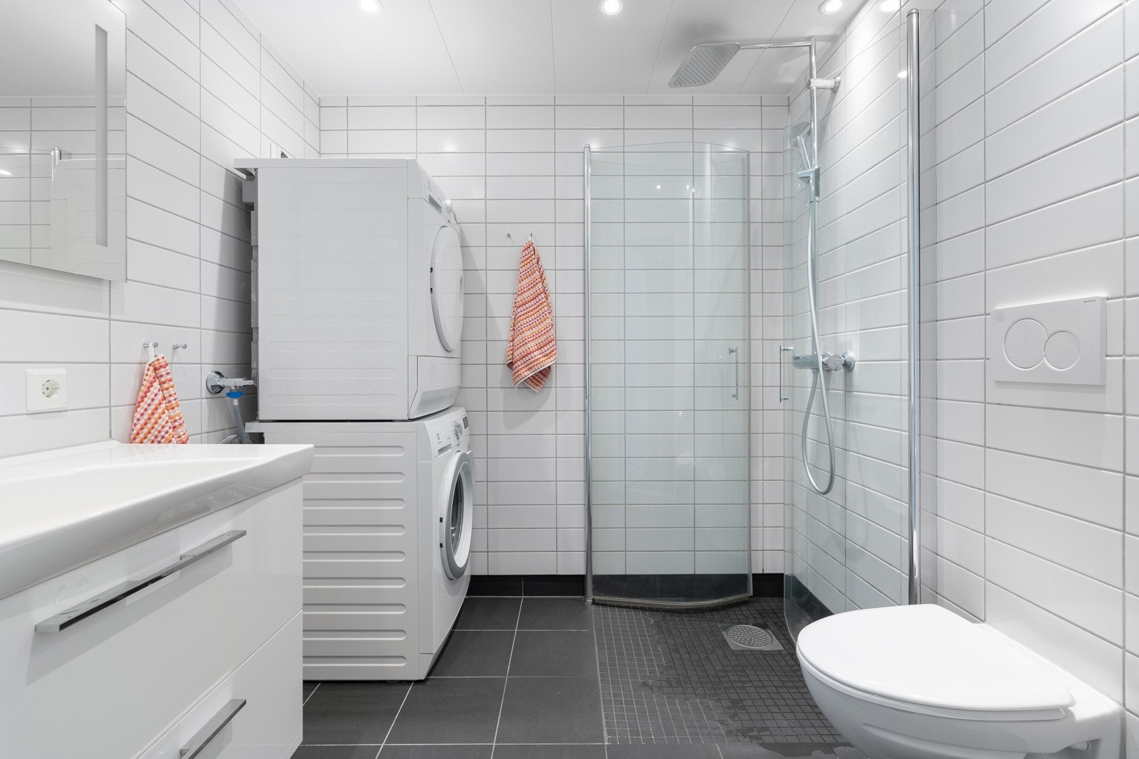 Stort flislagt bad med dusjhjørne, vegghengt wc og opplegg for vaskemaskin og tørketrommel. Galleribilde