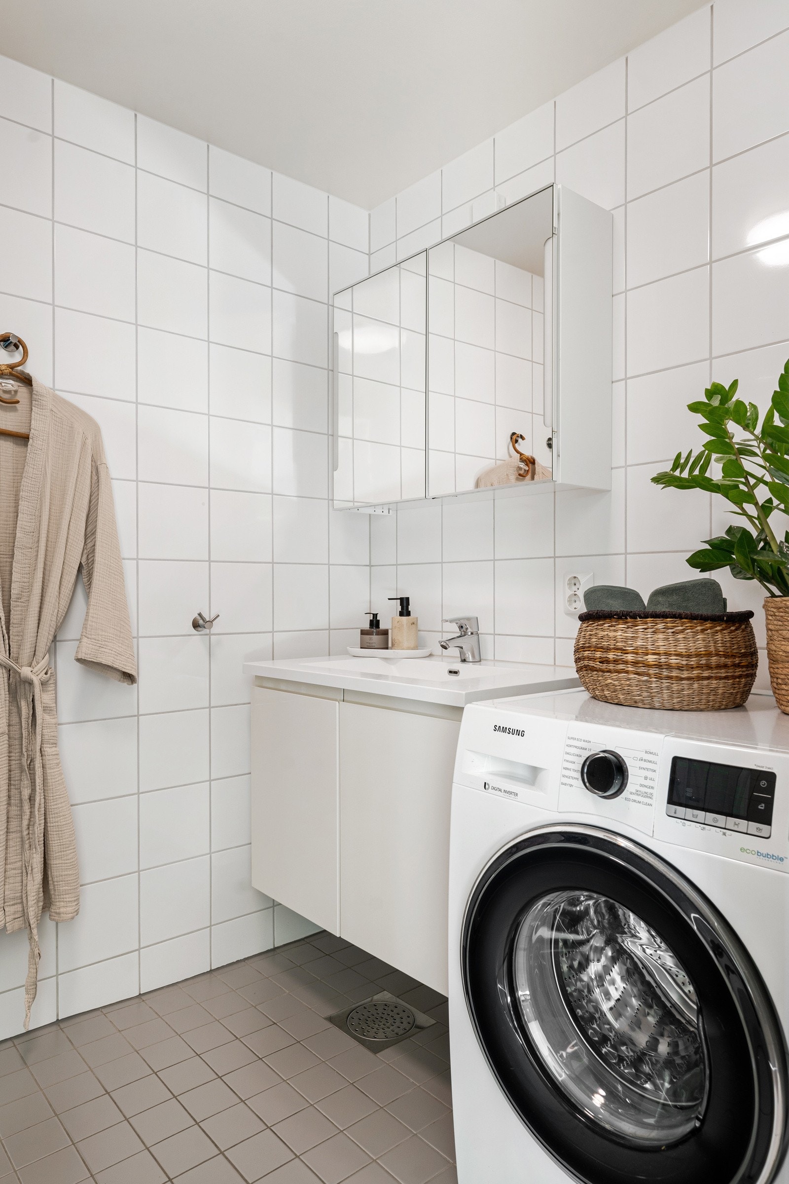 Badet er innredet med dusjhjørne, opplegg for vaskemaskin, vegghengt toalett og en praktisk baderomsinnredning med servant. Galleribilde