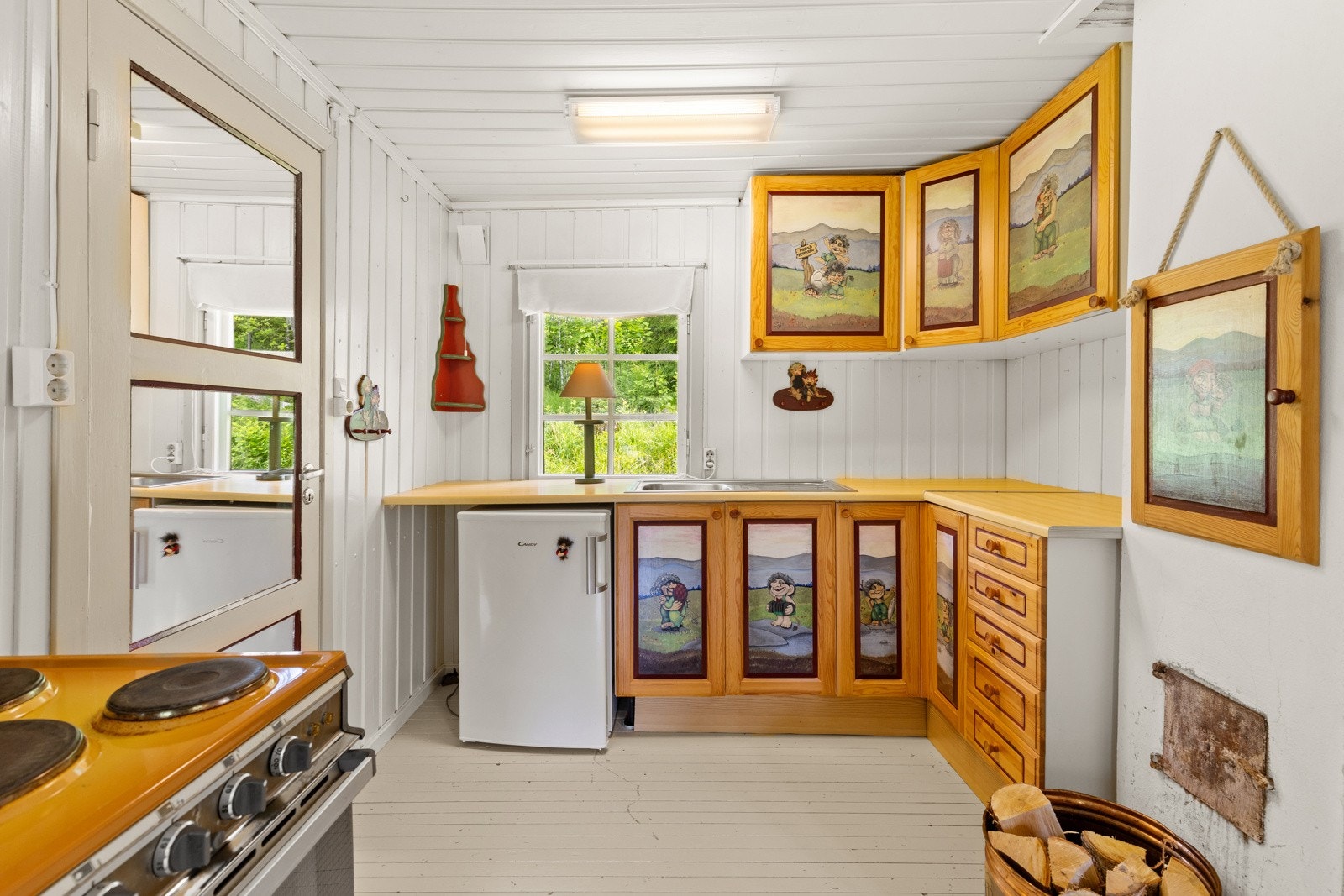 Kjøkkeninnredning med profilerte fronter malt med unike trollmotiver. Plass til frittstående kjøleskap og komfyr. Galleribilde