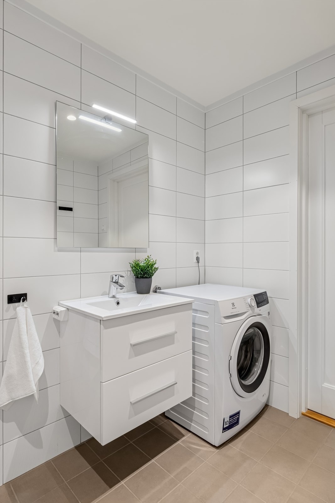 Badet er innredet med nedfelt servant, veggmontert toalett, dusjhjørne og opplegg for vaskemaskin. Galleribilde