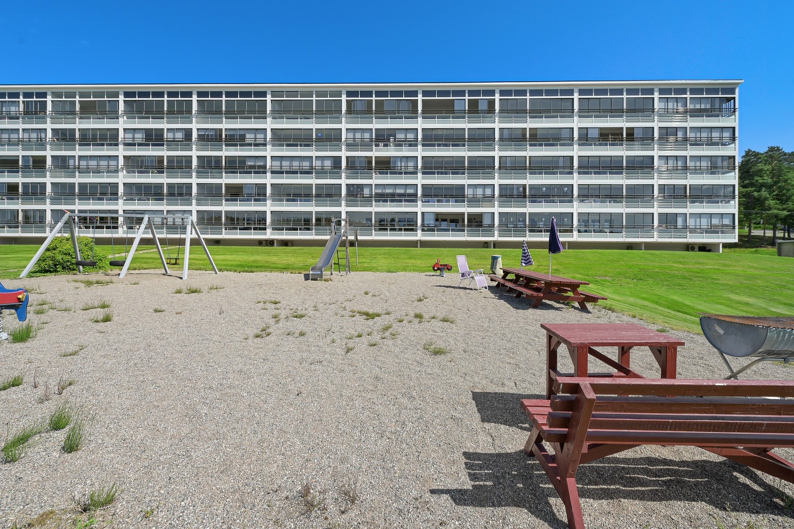 Barnevennlig område med lekeplass og stor gressplen foran bygget. Galleribilde