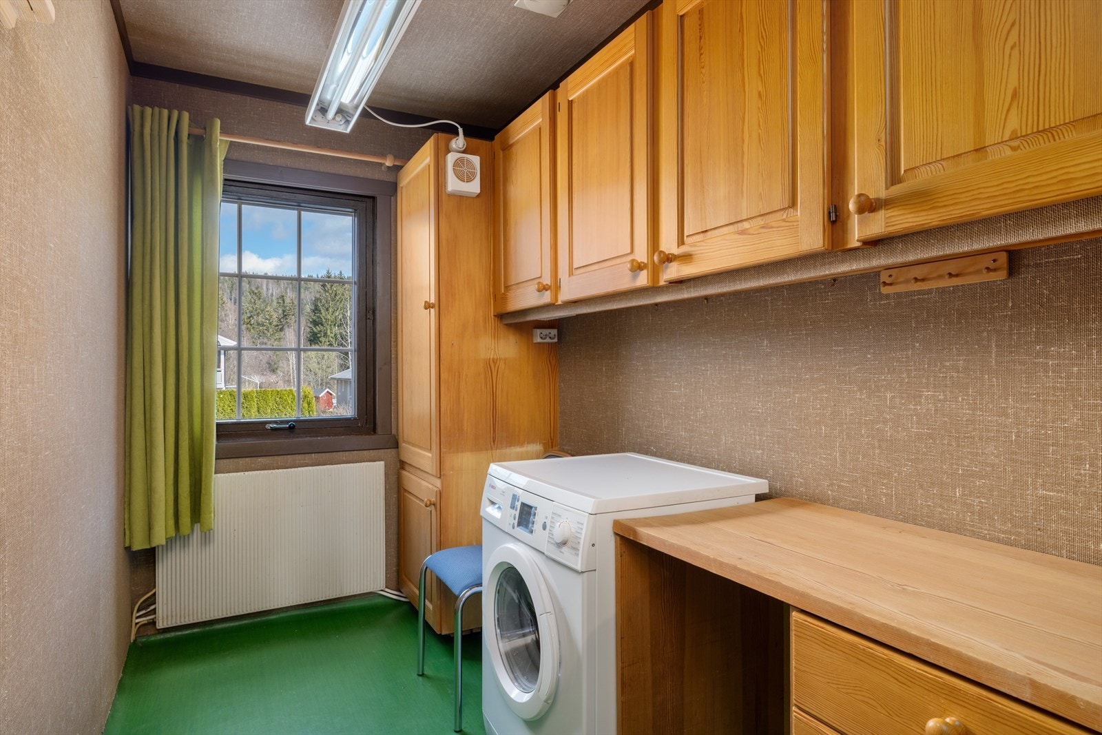 Vaskerom med platekledde vegg og himlingsflater, hovedsakelig tapetserte og vinylbelegg på gulv. Vaskerommet har innredninger med benkeplate og skap i heltre og opplegg for vaskemaskin. Galleribilde