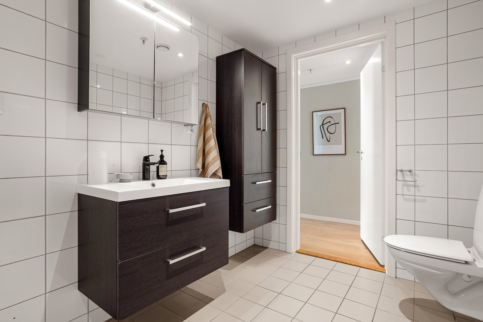 Innredningen består av en vegghengt servant med praktiske skuffer under, og en ovenpåliggende servant med ett-greps armatur. Speilskap med overlys gir ekstra oppbevaringsplass og god belysning til daglige gjøremål. Badet har i tillegg opplegg for vaskemas Galleribilde