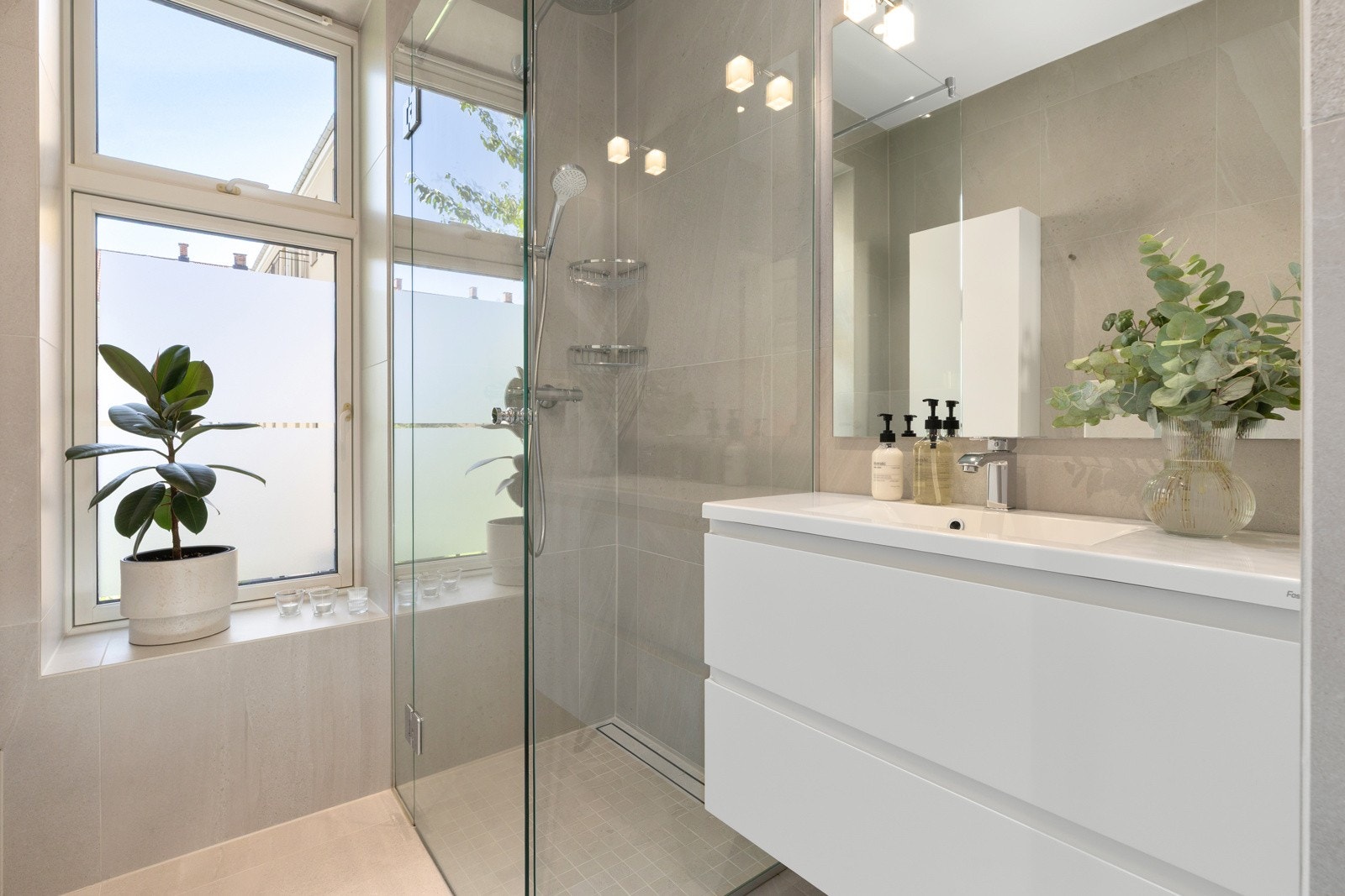 Det er gulvvarme, dusjhjørne med glassdører, servantinnredning med heldekkende benk, underskap, speil over, samt vegghengt toalett Galleribilde