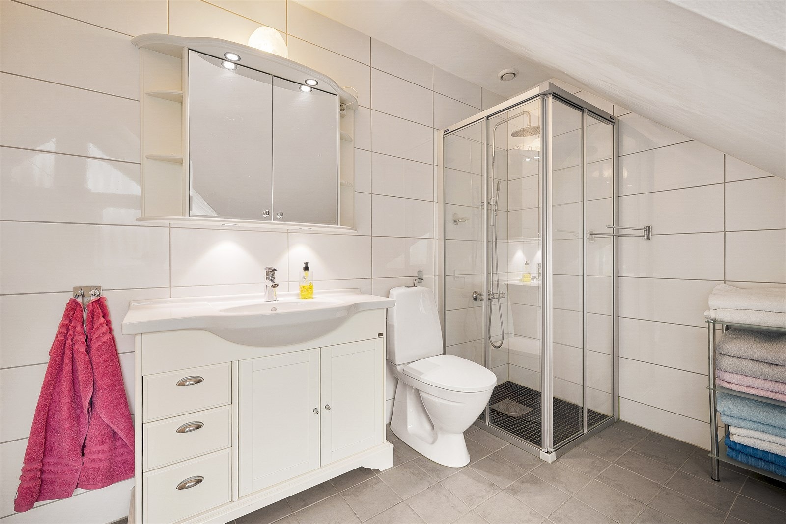 Badet er romslig og helfliset, med varme i gulvet. Det er innredet med dusjhjørne, toalett og baderomsmøbel med speil og belysning, samt plass til ekstra oppbevarings møbel. Galleribilde