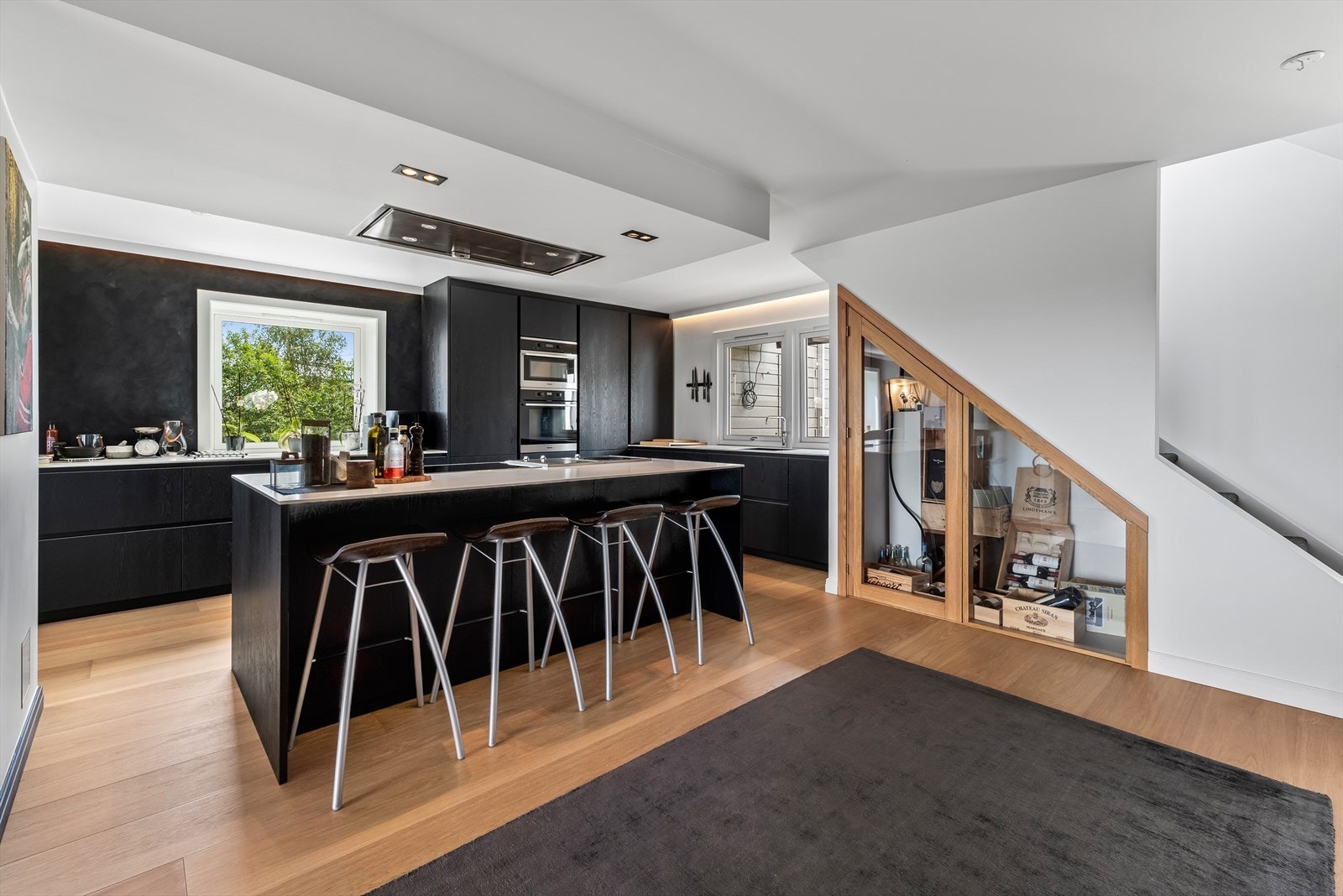 Praktisk og lekkert kjøkken med spiseplass på kjøkkenøy og vinrom under trappen. Galleribilde