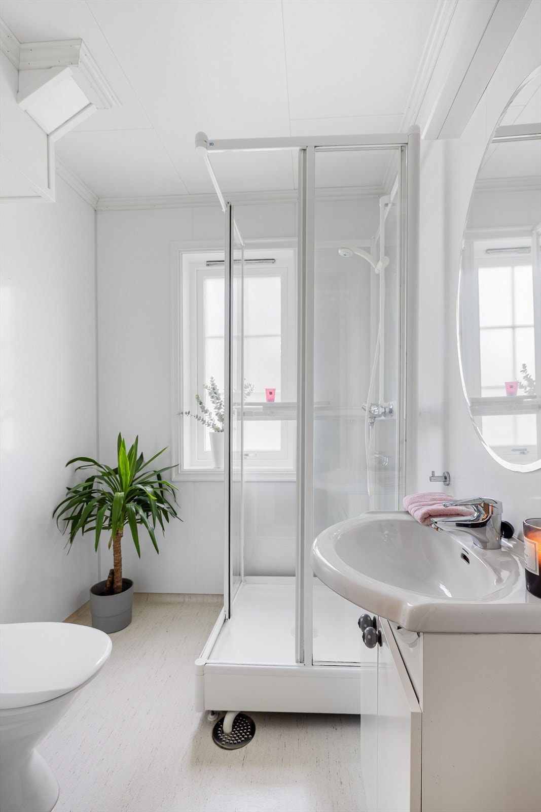Lyst baderom i 1. etasje med belegg på gulv og våtromsplater på veggene. Baderommet er utstyrt med servantskap, speil med belysning over, dusjkabinett og gulvstående toalett. Galleribilde