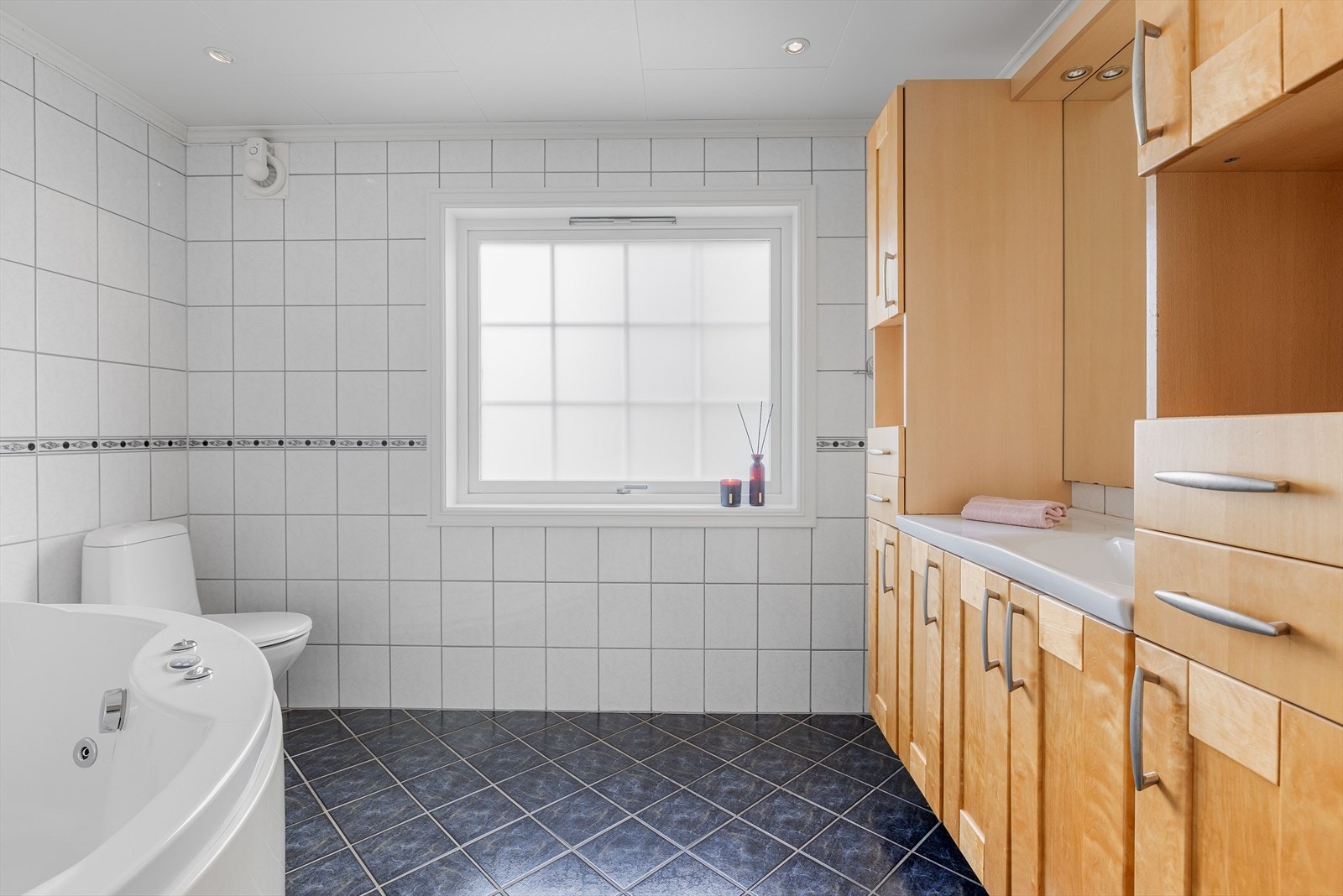 Lyst og tidløst baderom med fliser på gulv og vegger, deilig gulvvarme, downlights i himlingen og mekanisk avtrekksvifte. Galleribilde
