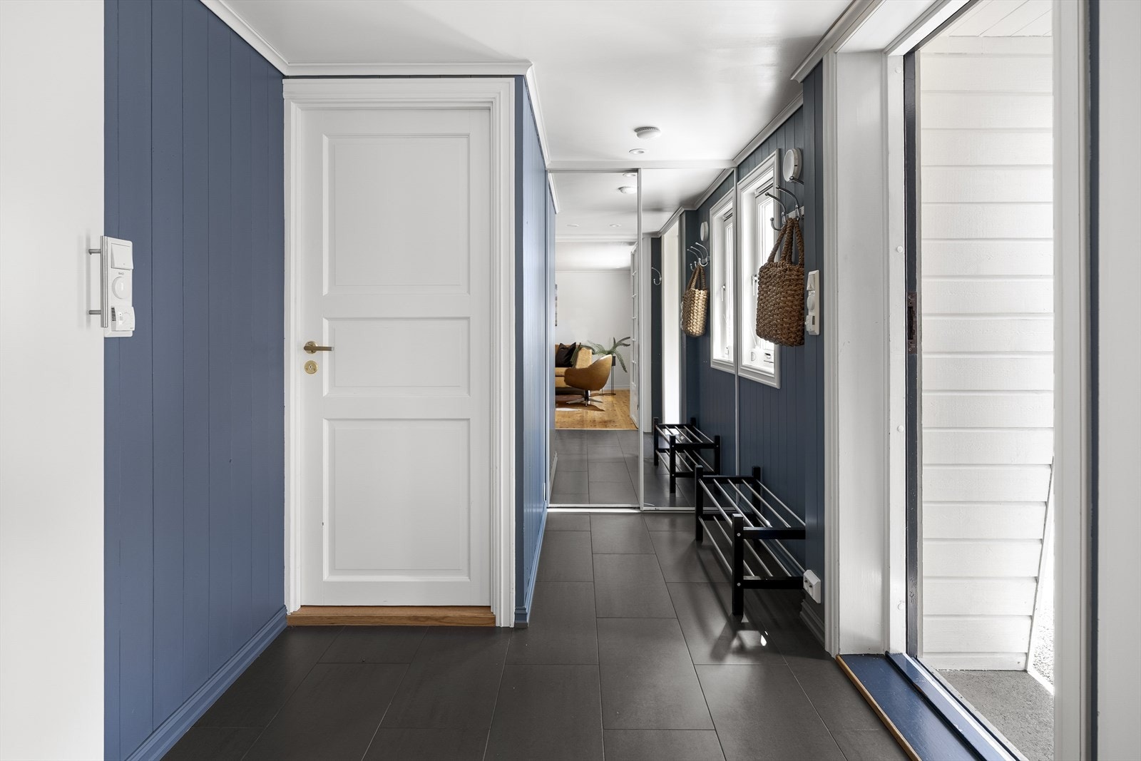 Innbydende entré med fliser på gulv og malte veggpanel. Her er det plass til å henge fra seg og sette fra seg sko og yttertøy i skyvedørsgarderobe. Galleribilde