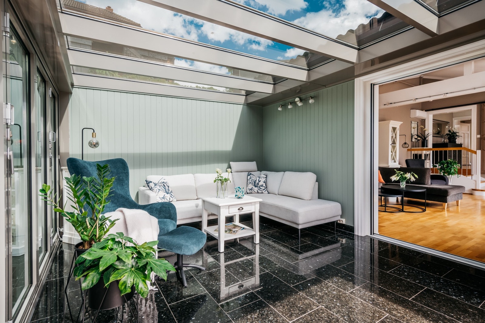 Lyset strømmer inn via glasstaket, utestuen har belysning og varme under sorte gulvfliser. Galleribilde