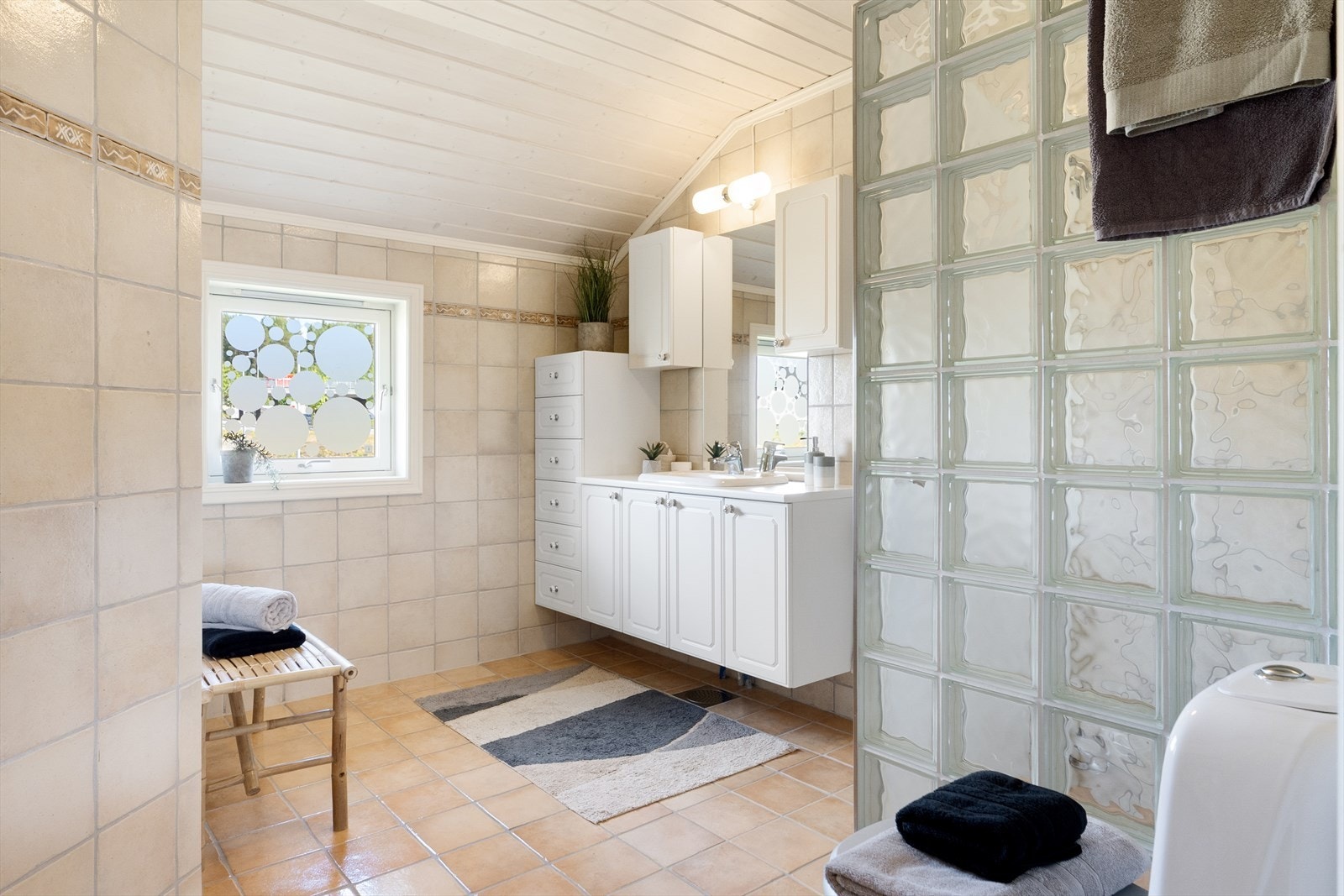 Flislagt bad - innredet med servantskap, gulvmontert toalett, dusjhjørne i glassbyggerstein med glassdør. Galleribilde