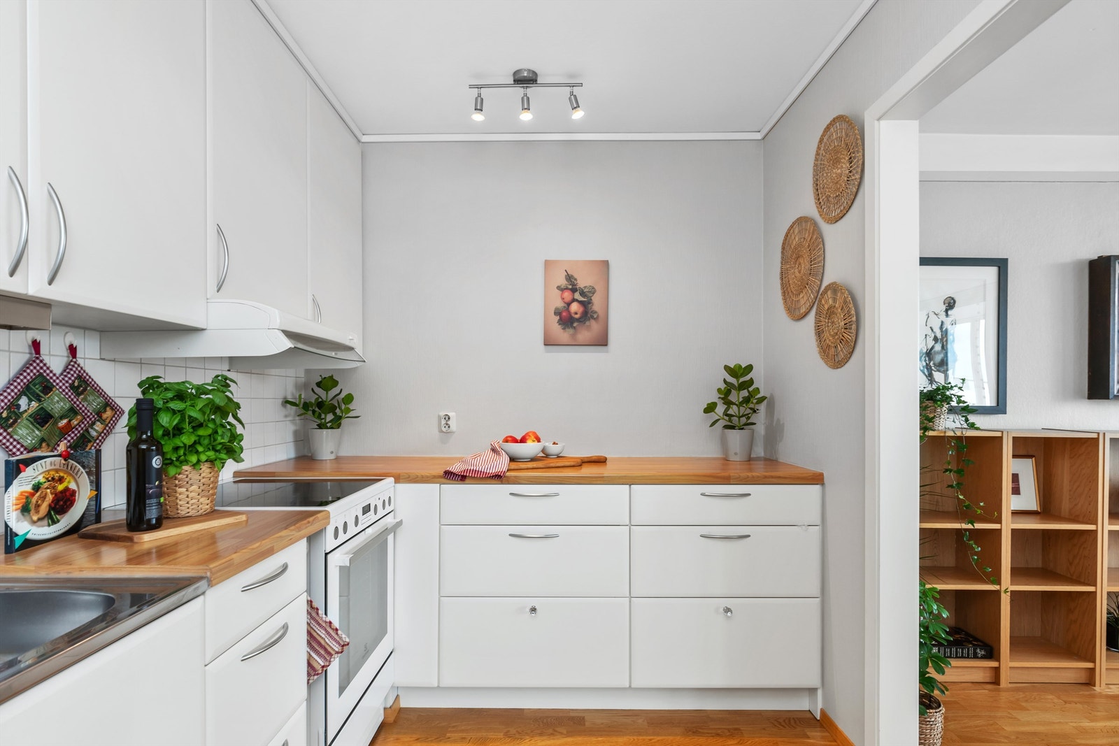 Lyst og funksjonelt kjøkken med hvite fronter og benkeplate i heltre som gir en varm kontrast. Kjøkkenet er godt utnyttet med rikelig skapplass og
komfyr. Galleribilde