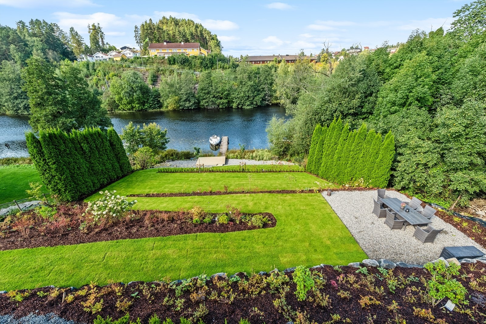 Tomten er pent opparbeidet med gressplen og beplantninger på flere nivåer ned til elven samt gruset innkjørsel og gårdsplass. Galleribilde