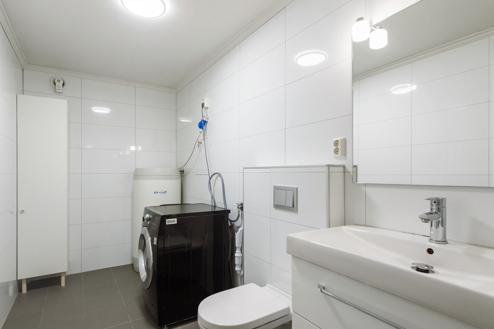 Rommet har et veggmontert toalett, en baderomsinnredning med heldekkende servant, speil med overliggende lys, dusj med innfellbare dusjdører og opplegg til vaskemaskin. Galleribilde