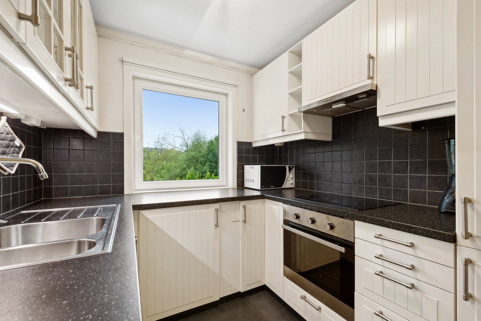 Kjøkkenet har en innredning fra 2015 med profilerte fronter, laminat benkeplate med nedfelt oppvaskkum, fliser på vegg over benk, lys under overskap og ventilator. Galleribilde