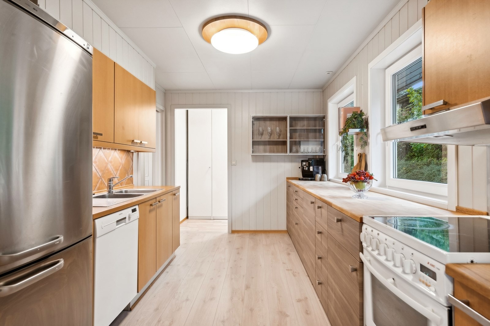 Innredningen har finerte fronter, laminat benkeplater, nedfelt oppvaskkum, ventilator, fliser over deler av benk og belysning under overskap. Galleribilde