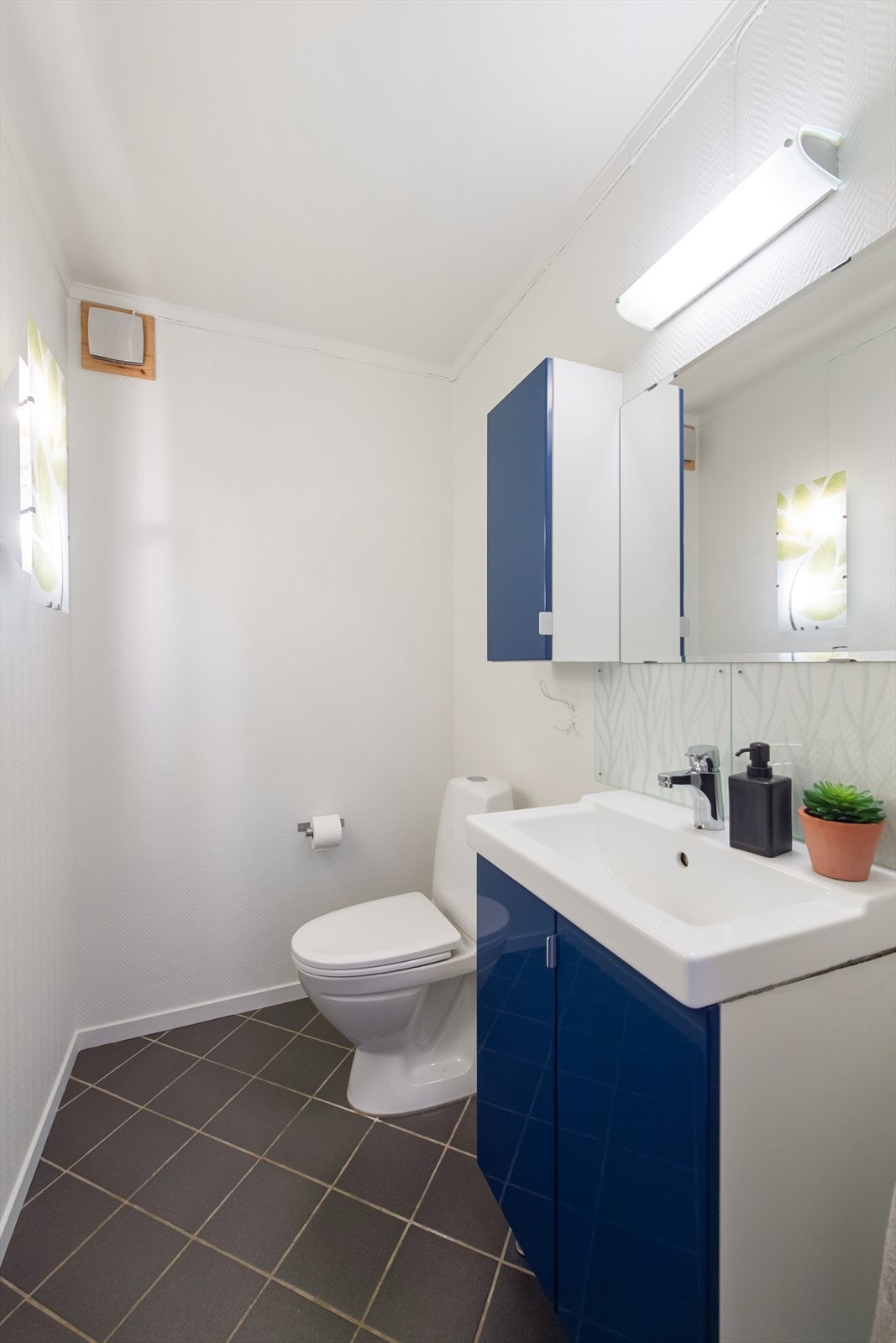 Toalettrommet har flislagt gulv, baderomsinnredning, speil med overliggende lys og toalett. Galleribilde