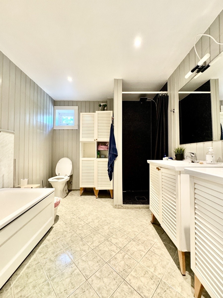 Hovedbadet i første etasje, eldre bortsett fra dusjnisjen med mosaikkflis. Ellers malt. Badekar, dusjnisje, to servanter. Varmekabler. Downlights. Galleribilde