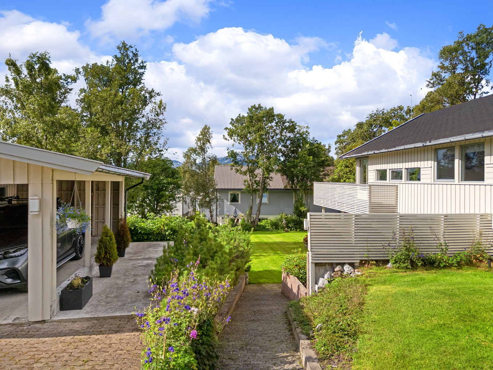 Boligen ligger i et etablert villaområde med store tomter, og har lett adkomst med parkering i garasje, carport og i tillegg plass for biler i innkjørsel.