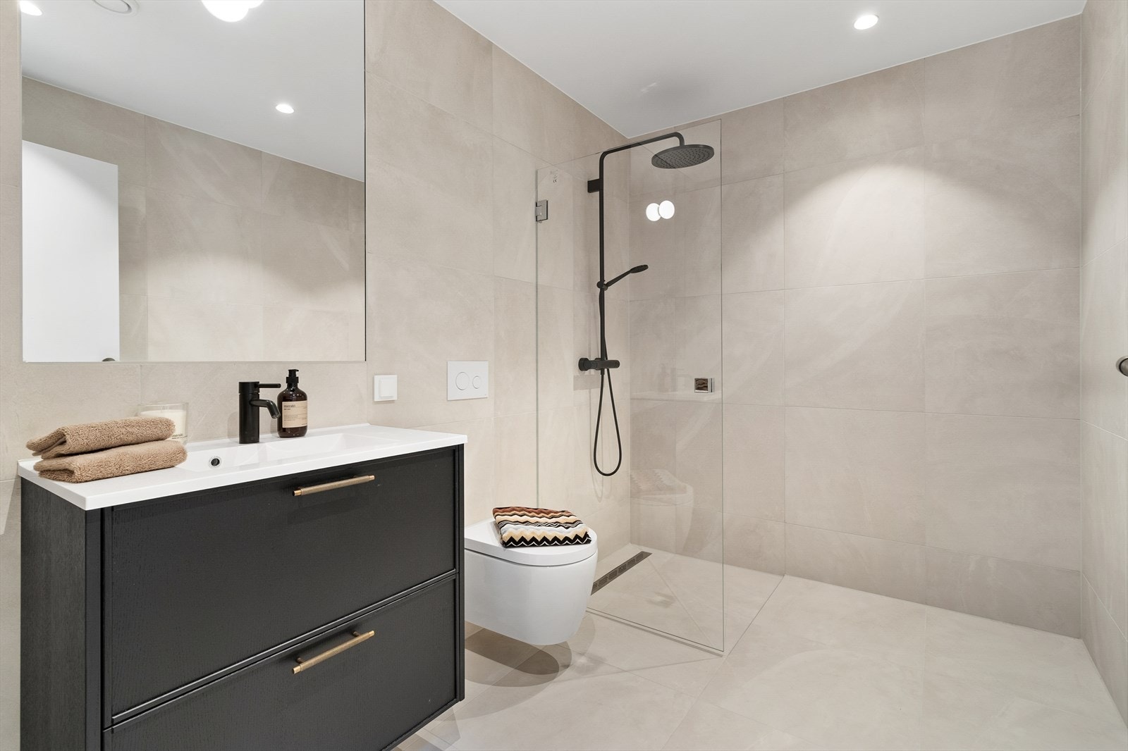 Bad i kjeller er helfliset med innfelte downlights i himling og varmekabler i gulvet. Her er det et praktisk dusjhjørne, servant med speil over og veggmontert toalett. Galleribilde