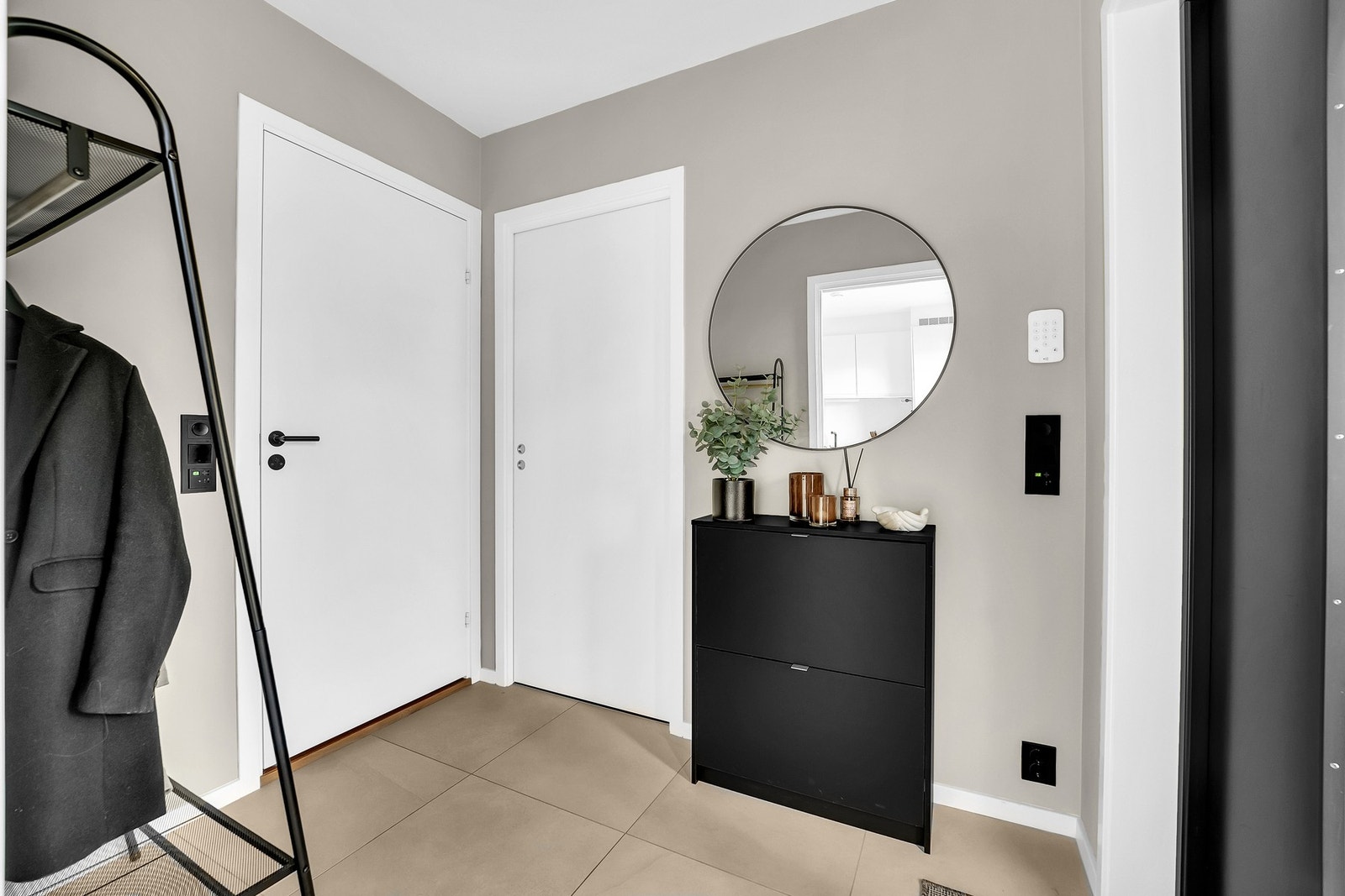 Du ønskes velkommen inn i en lysmalt entré med slette vegger malt i en beige tone, som står fint til de praktiske og slitesterke flisene på gulvet. Galleribilde