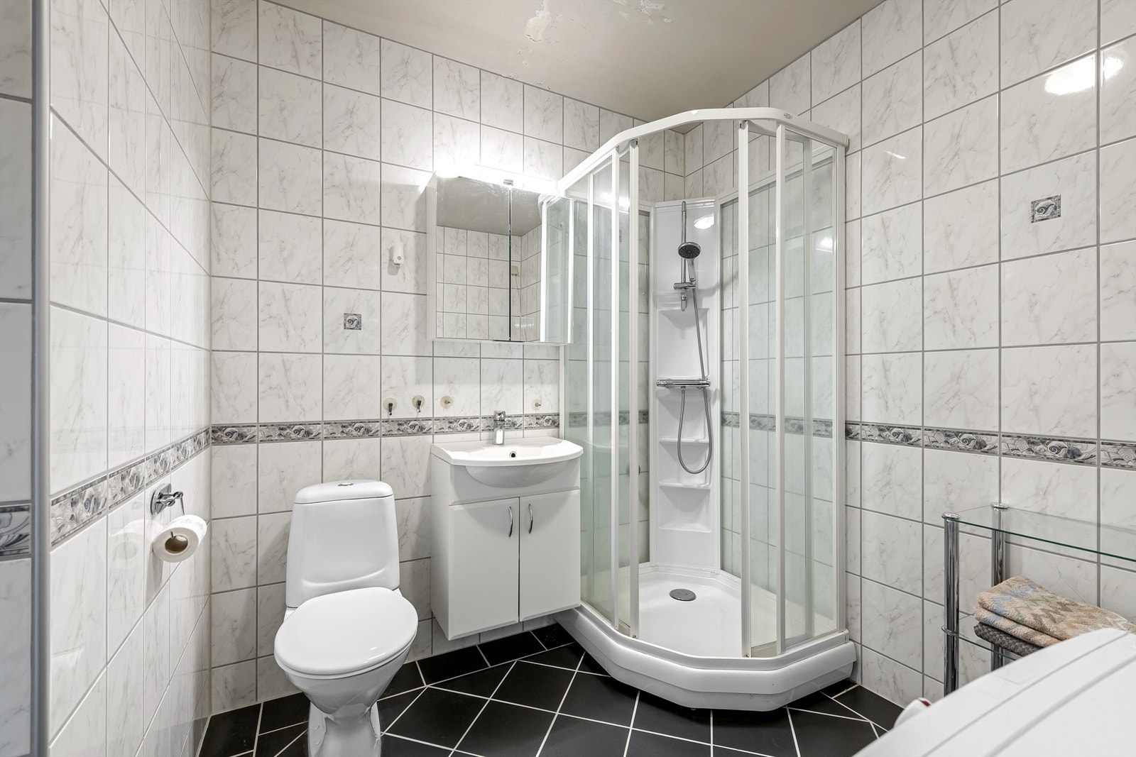 Badet har gulvmontert toalett, servantinnredning, speilskap, dusjkabinett og opplegg for vaskemaskin Galleribilde