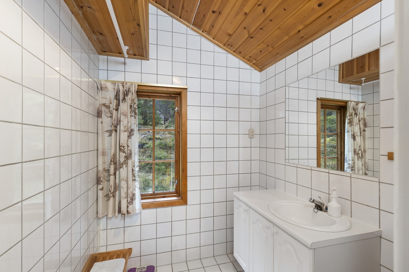 Flislagt bad med varmekabler i gulvet, dusjkabinett og servant med seksjon, samt speil på veggen. Over servanten er det innfliset speil. Galleribilde