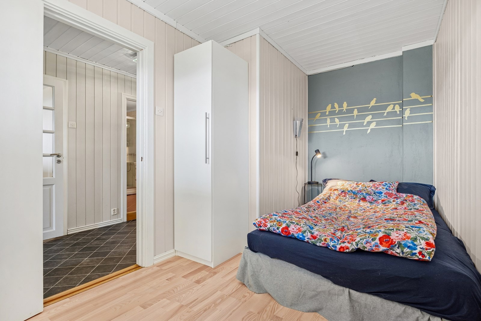Soverom med malt panel på vegger, en malt murvegg/gipsplate, ask parkettgulv, garderobeskap og Mill panelovn med glassfront. Galleribilde