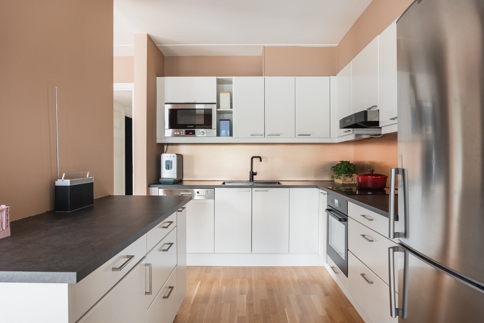 Innholdsrikt kjøkken utstyrt med mekanisk avtrekksvifte, kjøleskap og integrert oppvaskmaskin, platetopp, stekovn og mikroovn. Galleribilde