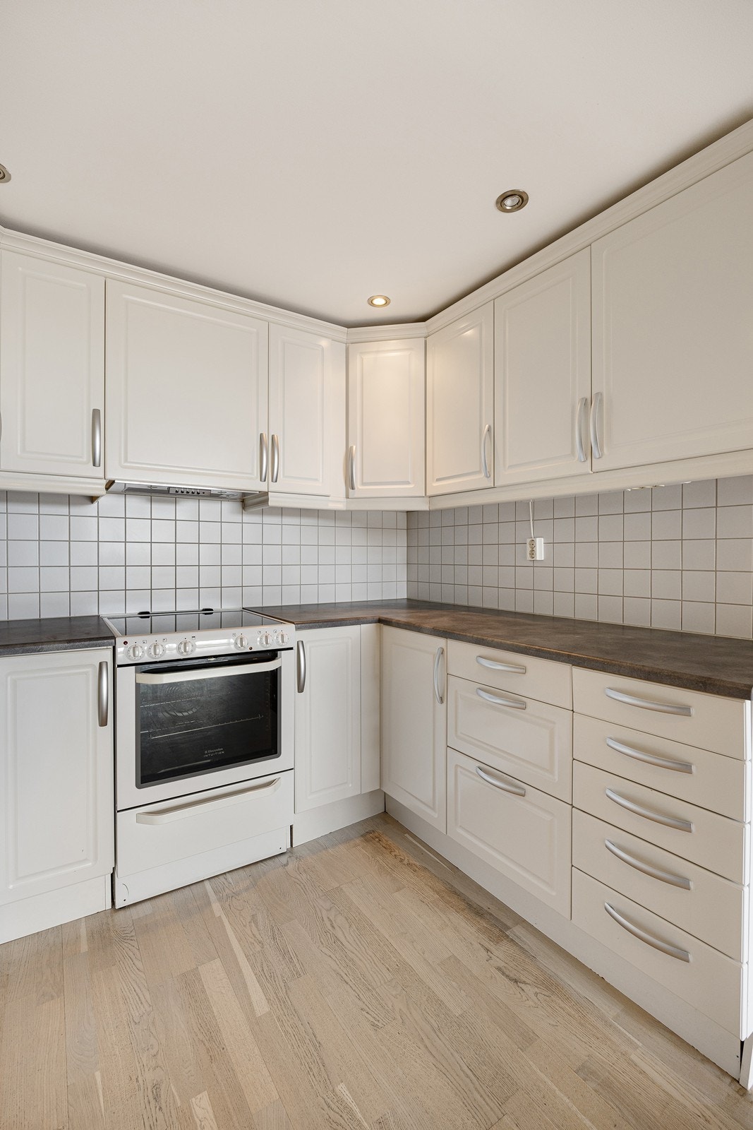 Kjøkkeninnredningen har hvite, profilerte fronter og laminert benkeplate. Det er avsatt plass til frittstående hvitevarer. Galleribilde