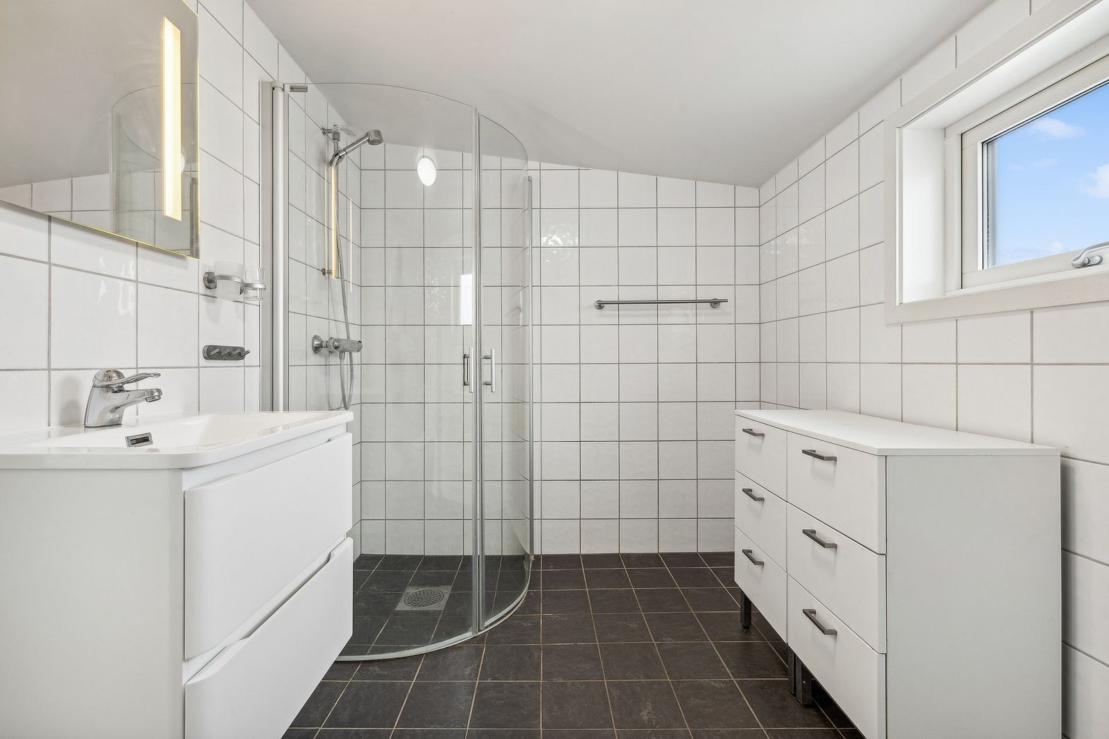 Badet er innredet med vegghengt toalett, vask i seksjon, speil med belysning og dusjhjørne. Galleribilde