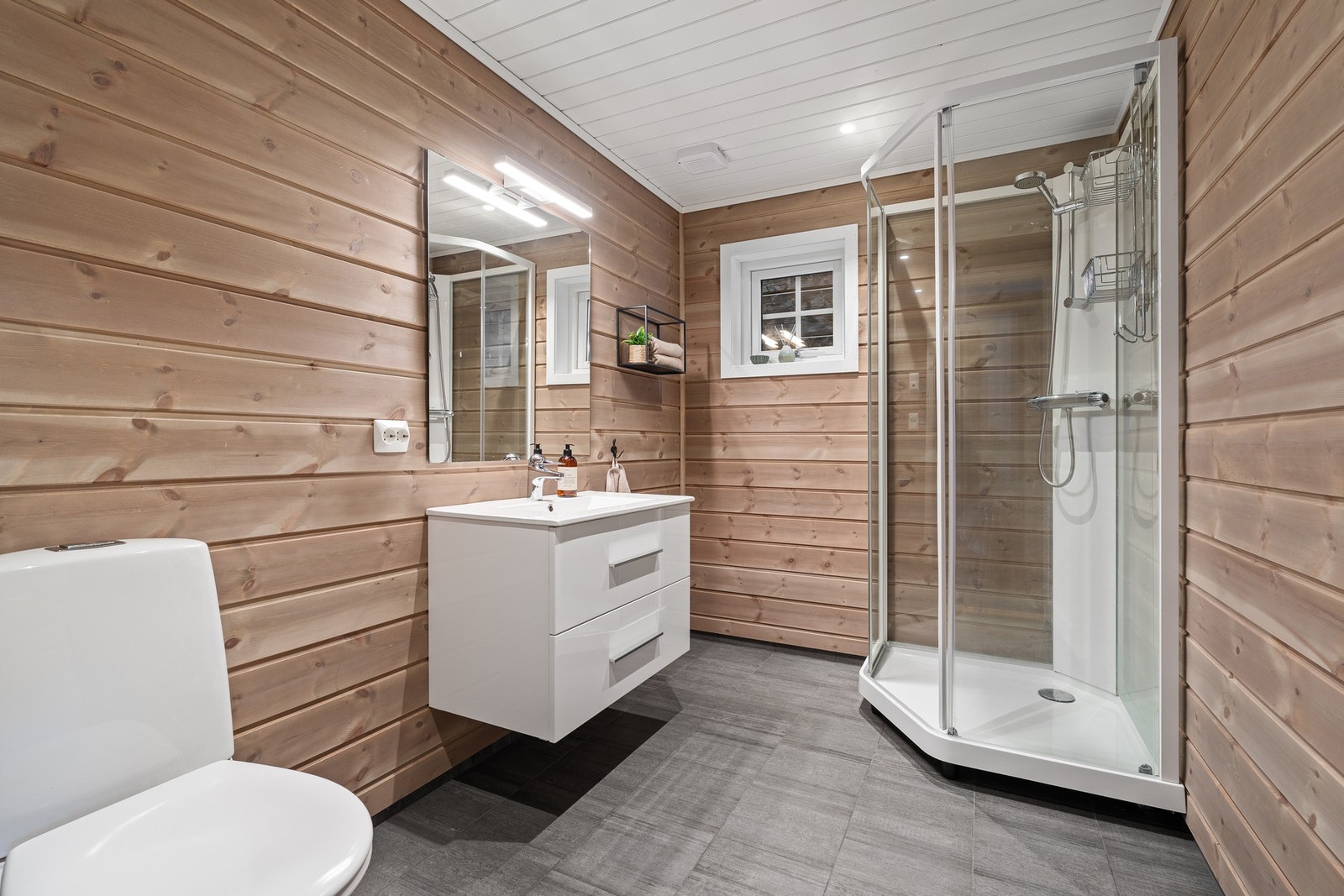 Bad med dusjkabinett, vegghengt servant og toalett. Flislagt gulv og panel på veggene. Galleribilde