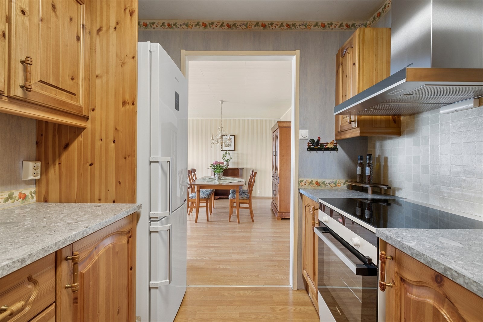 Velholdt kjøkken med åpning mot spisestuen med kjøkkeninnredningen som har profilerte fronter og inkluderer benkeskap og overskap for praktisk oppbevaring. Galleribilde