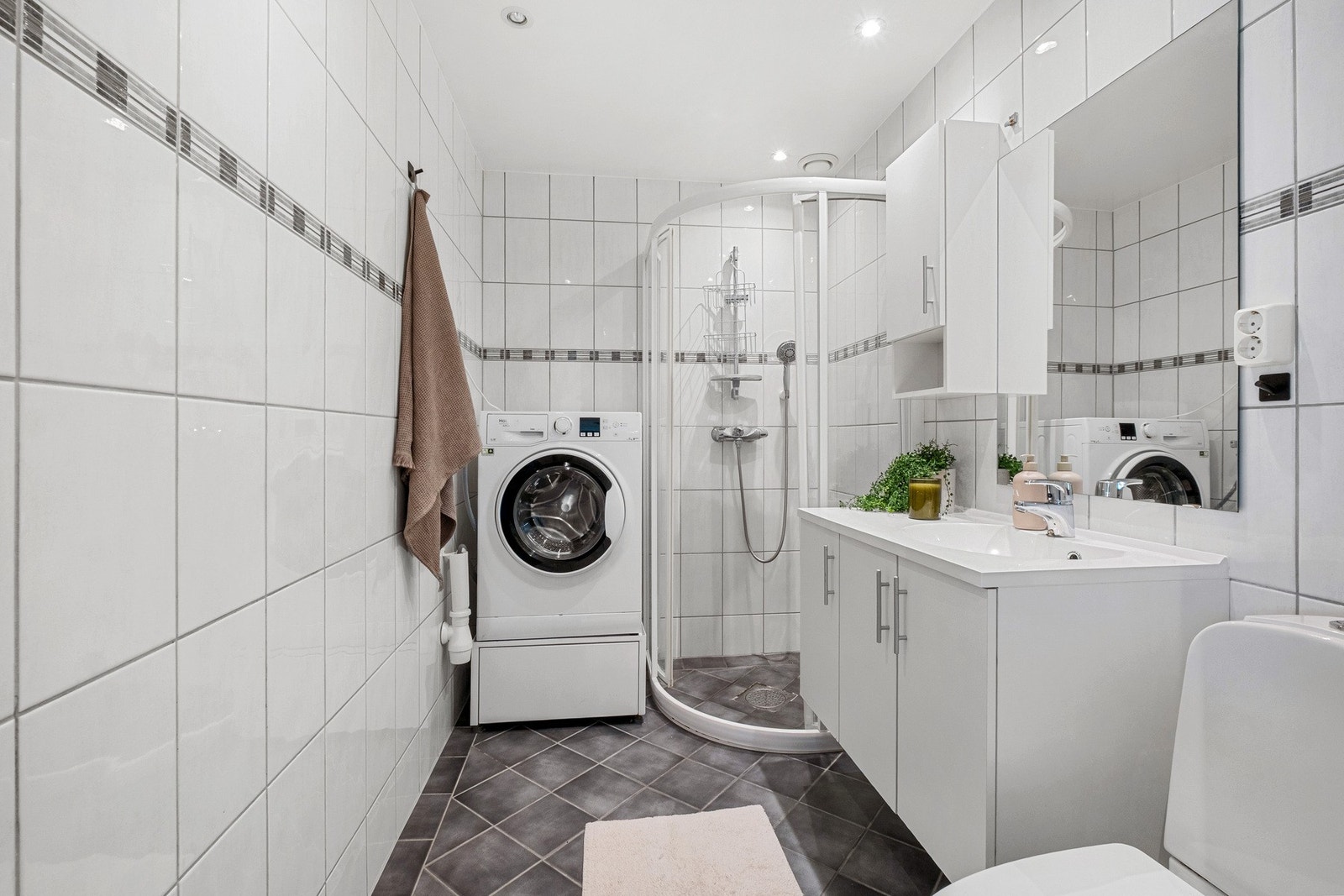 Flislagt bad i tidløs utførelse med dusjnisje, toalett, opplegg for vaskemaskin - og servantseksjon med speil. Galleribilde