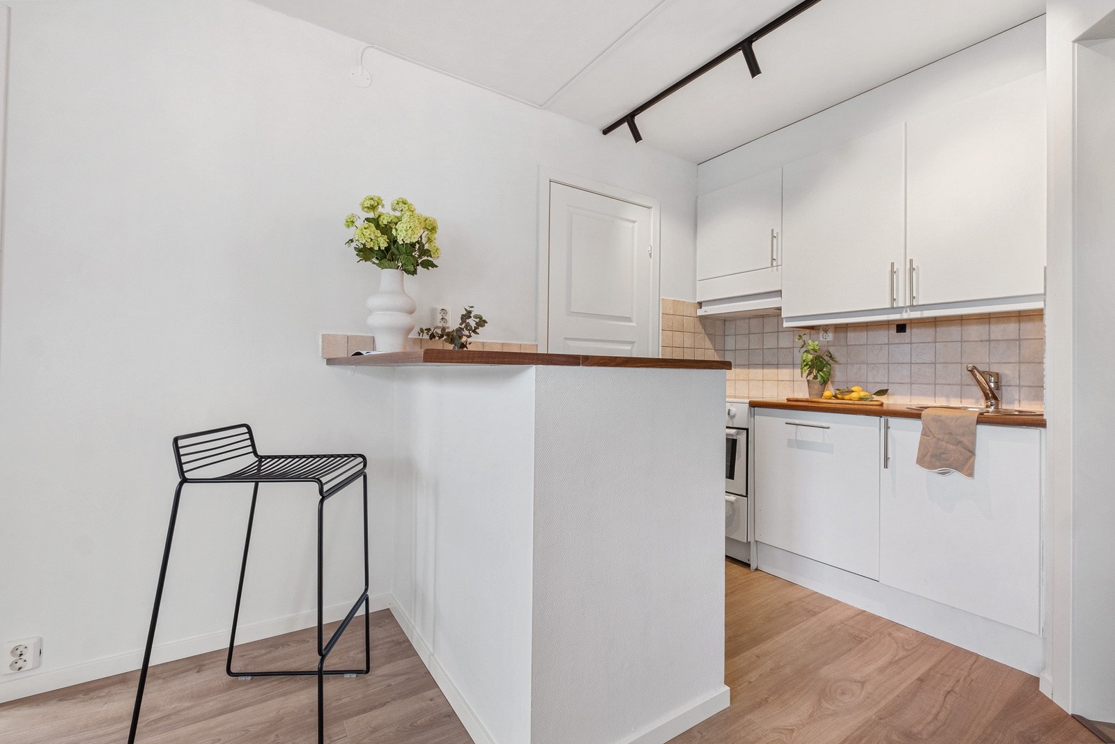 Tidløst kjøkken med hvite fronter og benkeplate i laminat. Fliser over benk med belysning. Galleribilde